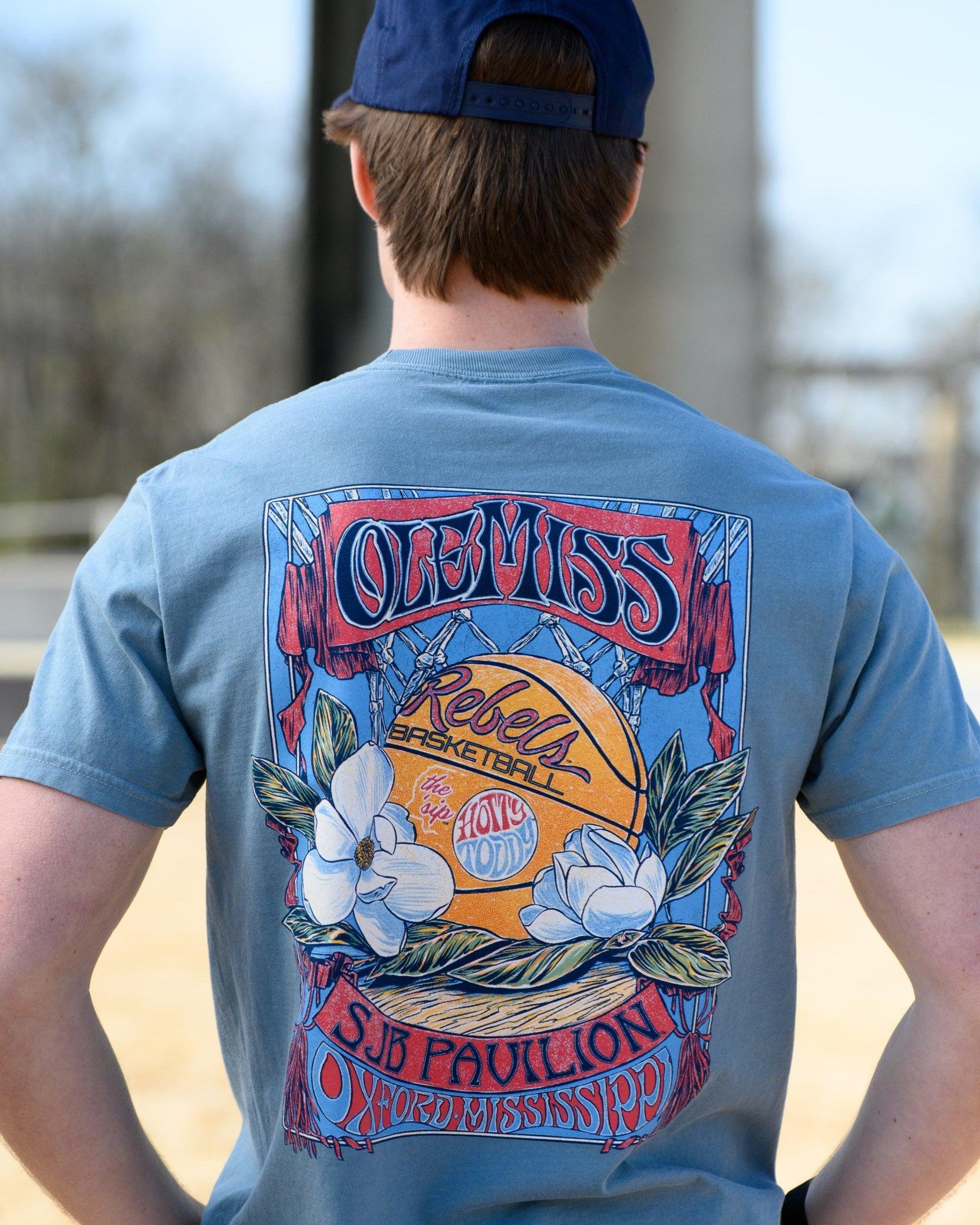 Ole Miss Dusty Light Blue T-Shirt with a basketball card style design featuring a basketball with magnolia flowers in between text “Ole Miss” and “SJB Pavilion”