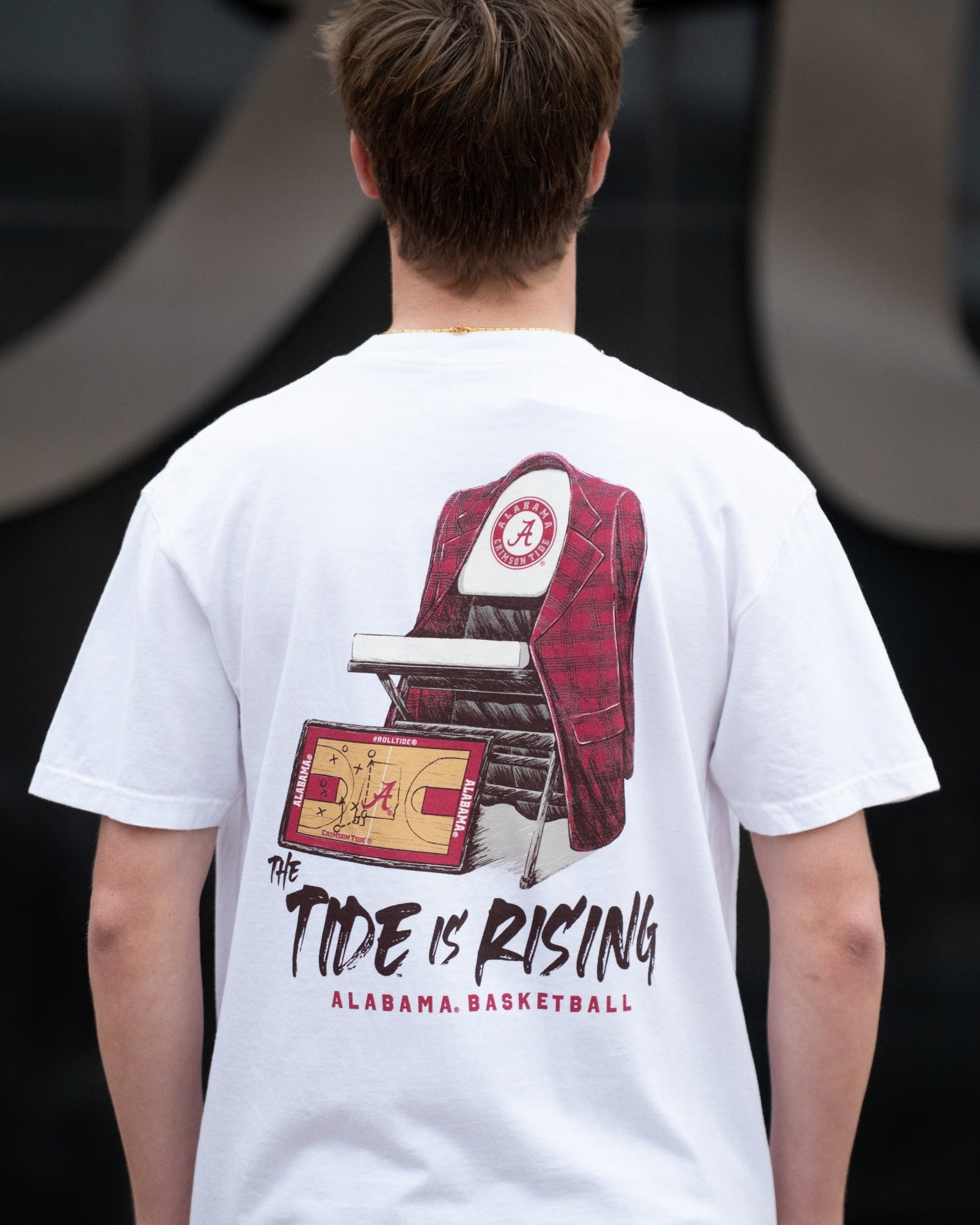University of Alabama White T-shirt with a Script A brand folding chair that has a red flannel hanging over the back and a play planning board leaning against it. Below, Black text reading “The Tide is Rising”