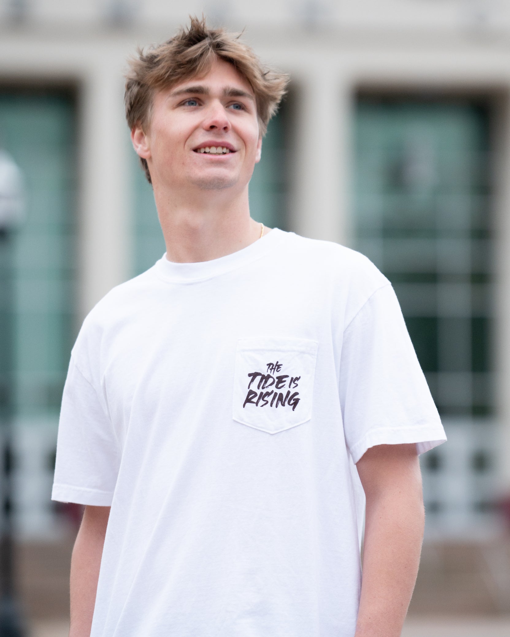 University of Alabama White T-shirt with a Script A brand folding chair that has a red flannel hanging over the back and a play planning board leaning against it. Below, Black text reading “The Tide is Rising”