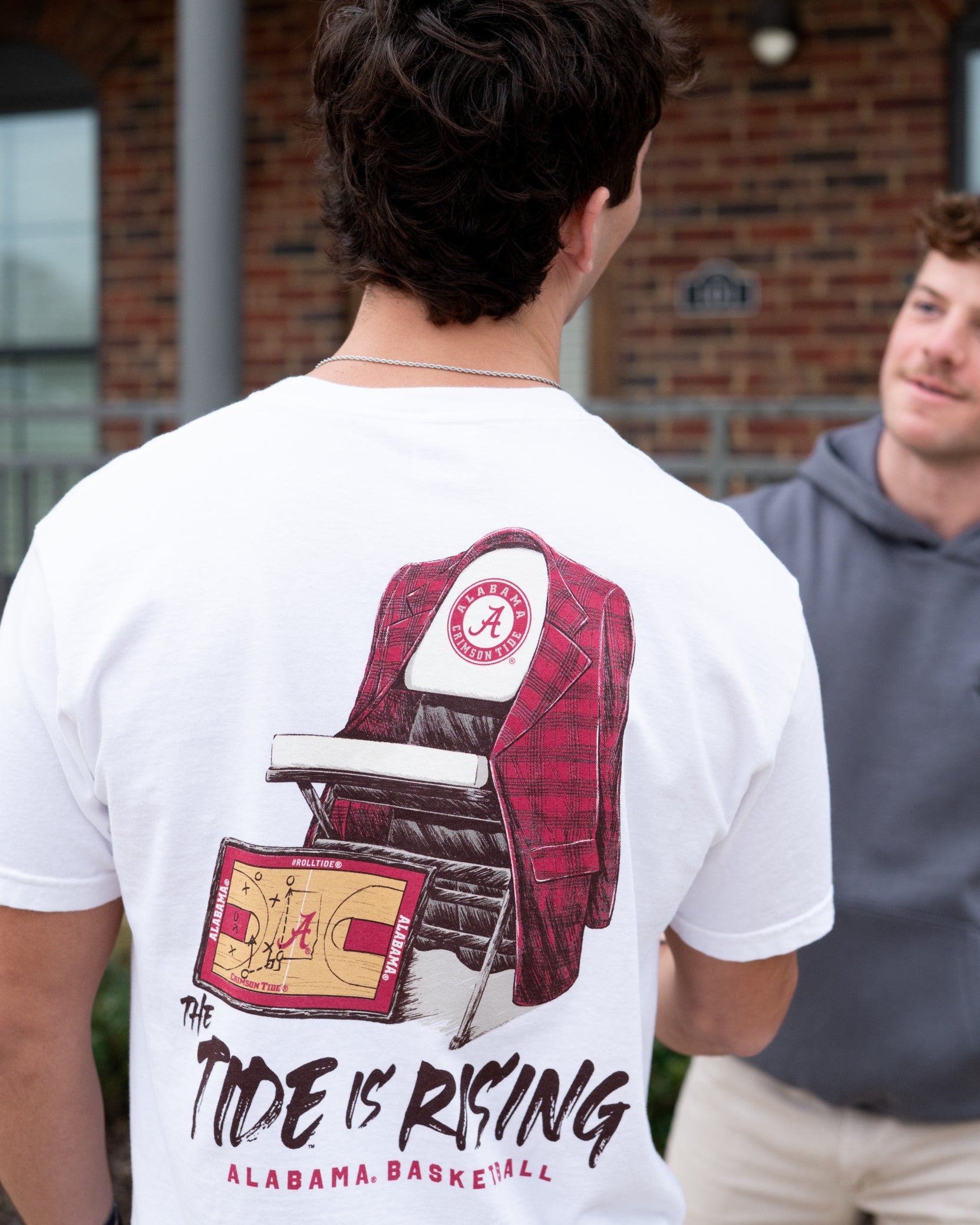 University of Alabama White T-shirt with a Script A brand folding chair that has a red flannel hanging over the back and a play planning board leaning against it. Below, Black text reading “The Tide is Rising”