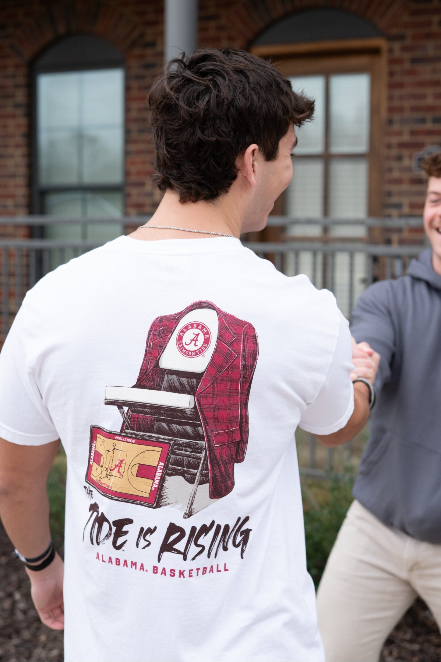 University of Alabama White T-shirt with a Script A brand folding chair that has a red flannel hanging over the back and a play planning board leaning against it. Below, Black text reading “The Tide is Rising”
