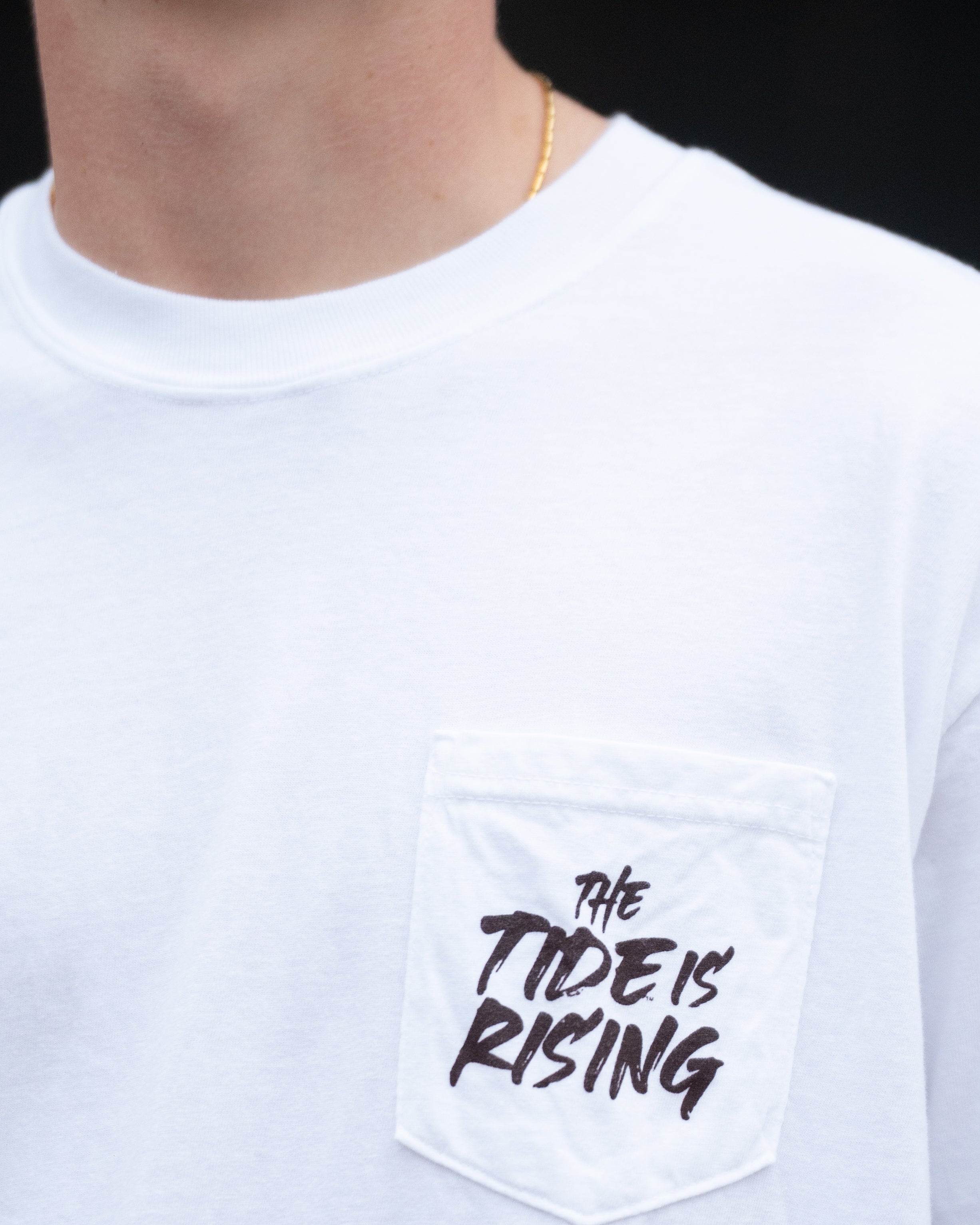 University of Alabama White T-shirt with a Script A brand folding chair that has a red flannel hanging over the back and a play planning board leaning against it. Below, Black text reading “The Tide is Rising”
