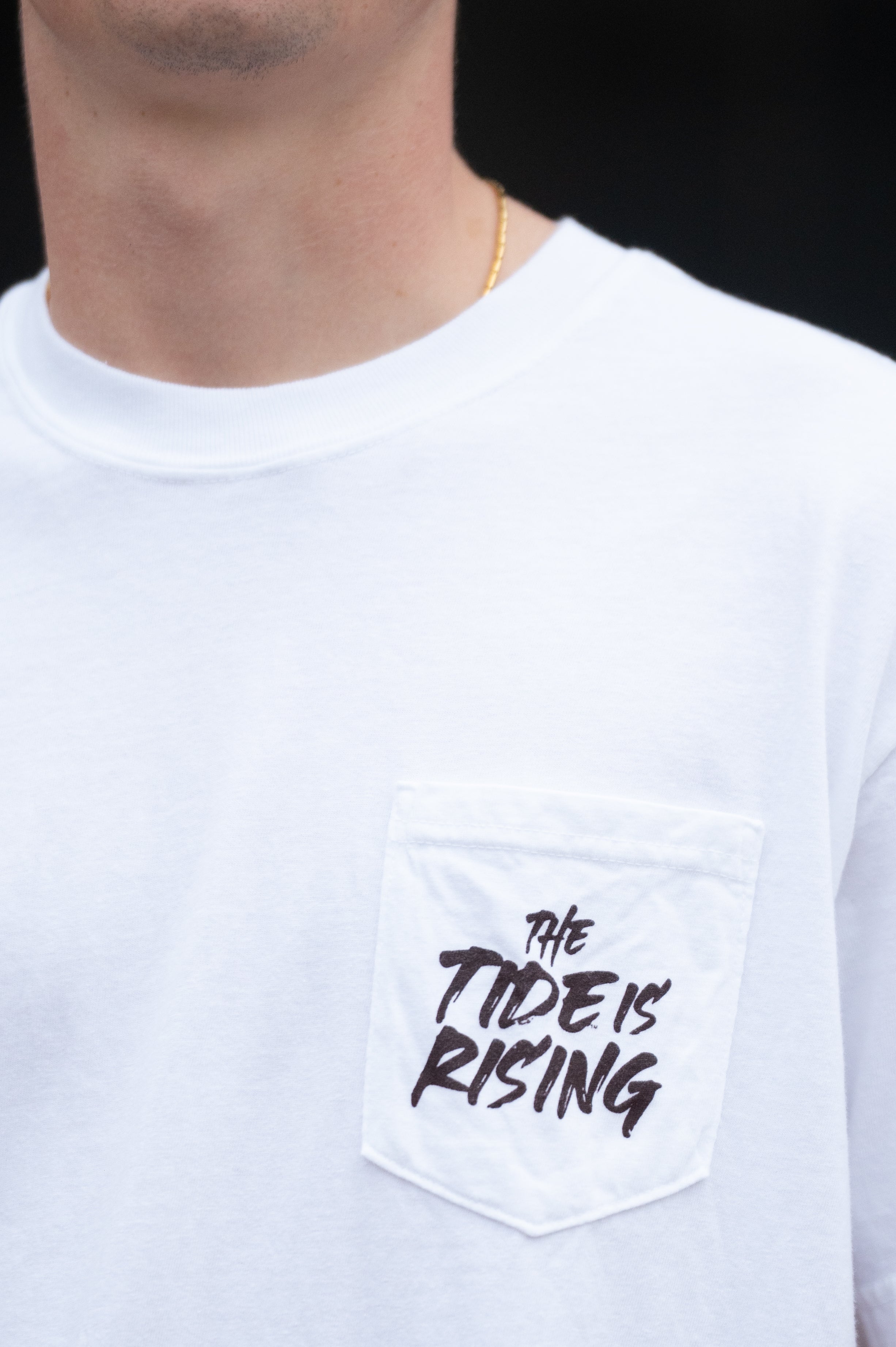 University of Alabama White T-shirt with a Script A brand folding chair that has a red flannel hanging over the back and a play planning board leaning against it. Below, Black text reading “The Tide is Rising”
