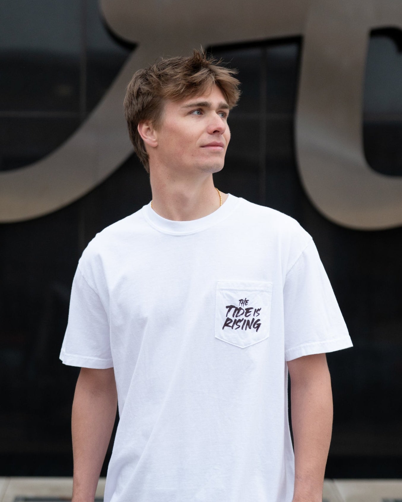 University of Alabama White T-shirt with a Script A brand folding chair that has a red flannel hanging over the back and a play planning board leaning against it. Below, Black text reading “The Tide is Rising”