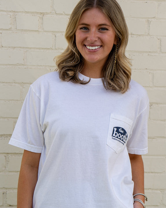 Woman wearing a white t-shirt with a logo, standing against a light brick wall.