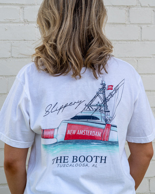 Person wearing a white t-shirt with a graphic design of a ship and text on the back, standing against a white brick wall.