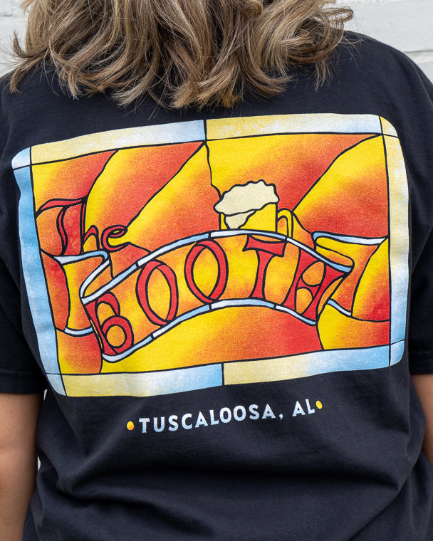 Person wearing a black t-shirt with a colorful graphic design on the back, featuring the word 'BOOTH' and 'Tuscaloosa, AL'.