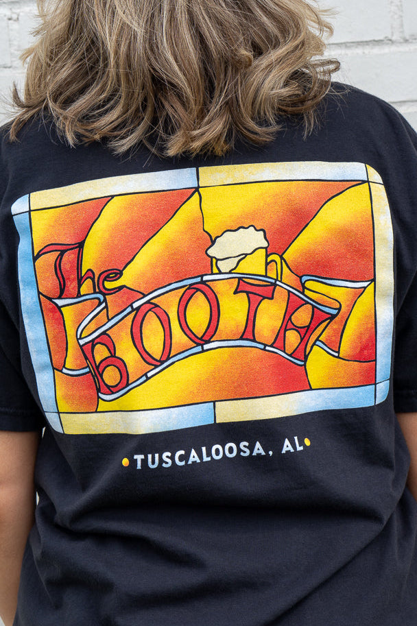 Person wearing a black t-shirt with a colorful graphic design on the back, featuring the word 'BOOTH' and 'Tuscaloosa, AL'.