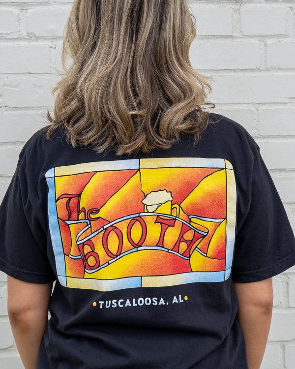 Person wearing a black t-shirt with colorful graphic design on the back, standing against a white brick wall.