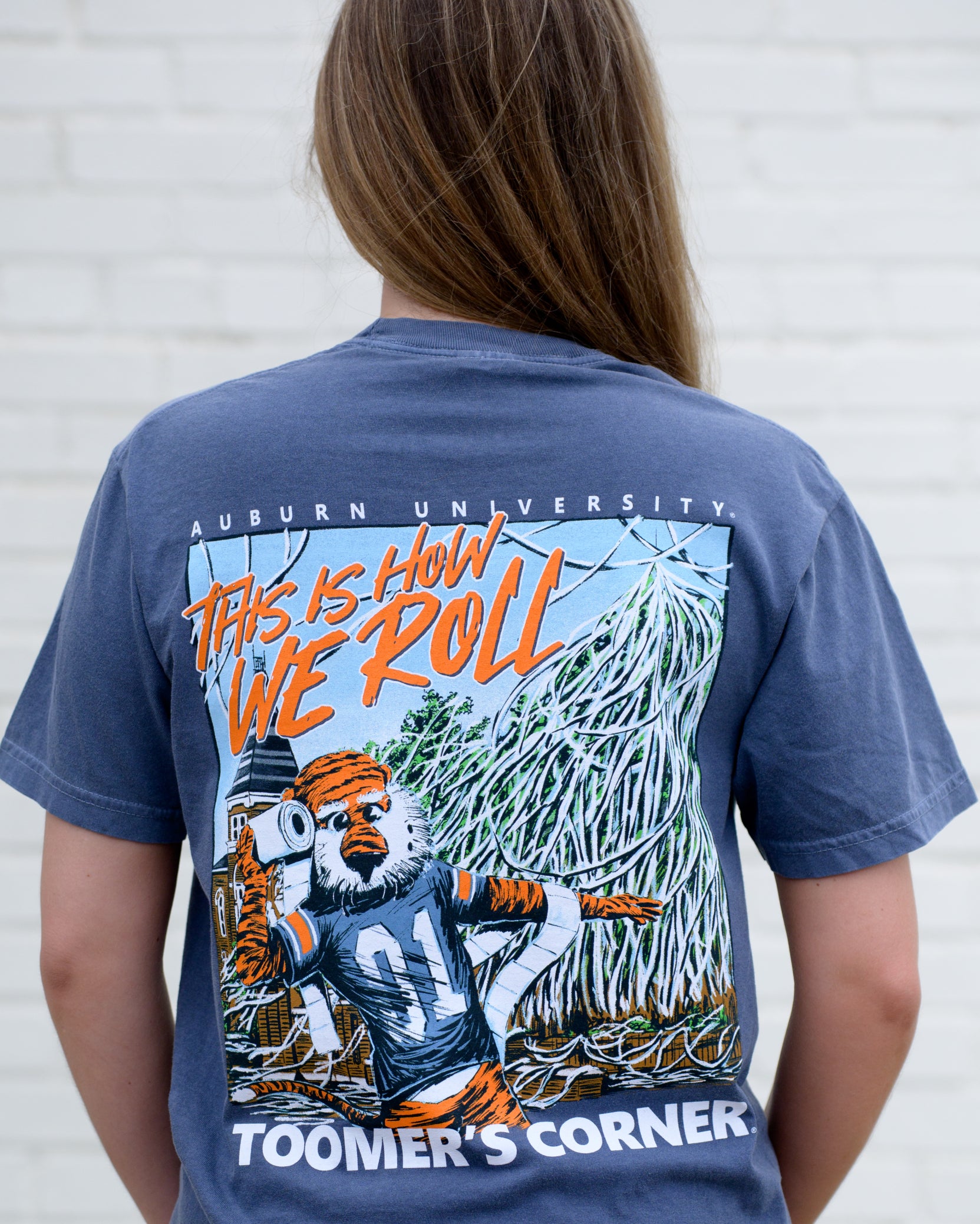 Auburn University Blue This is How We Roll T-Shirt featuring an illustration of Aubie rolling the Toomer's Corner Magnolias beneath Orange text "This Is How We Roll"
