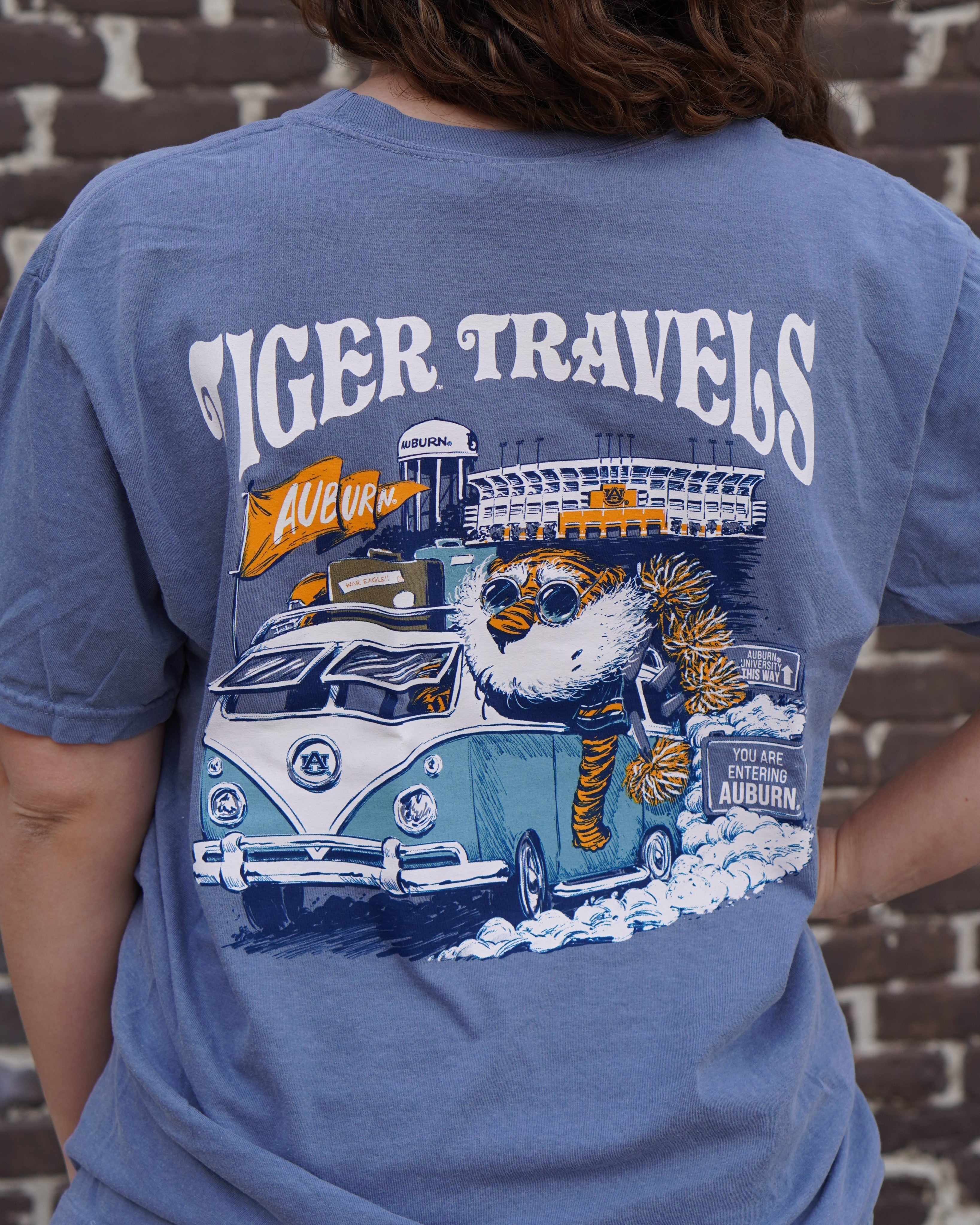 Auburn University Blue T-Shirt with 'Tiger Travels' text and an illustration of  Aubie in a VW Bus leaving the Auburn campus