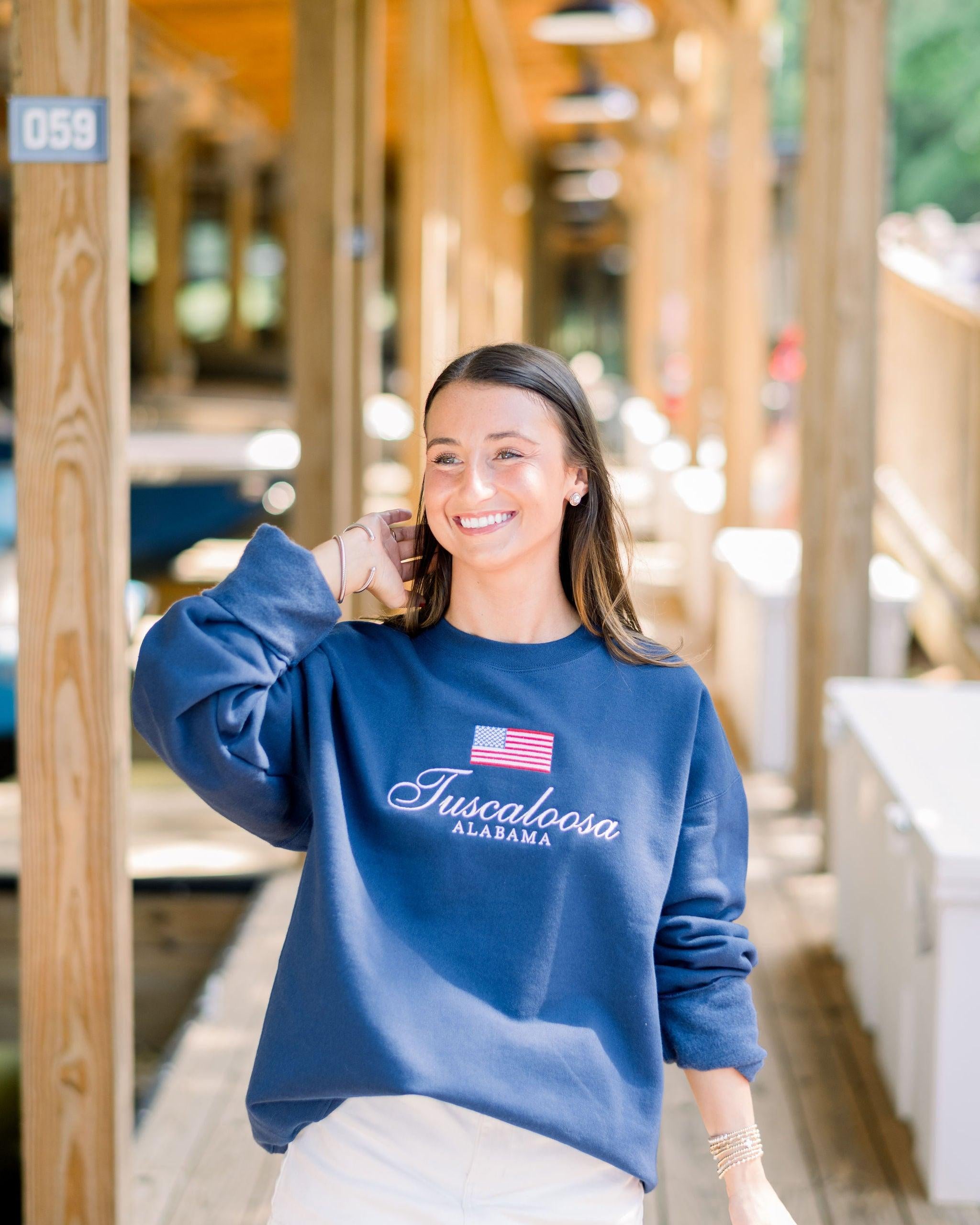 Local Merch Navy Crewneck with an embroidered American Flag above White embroidered text “Tuscaloosa Alabama”