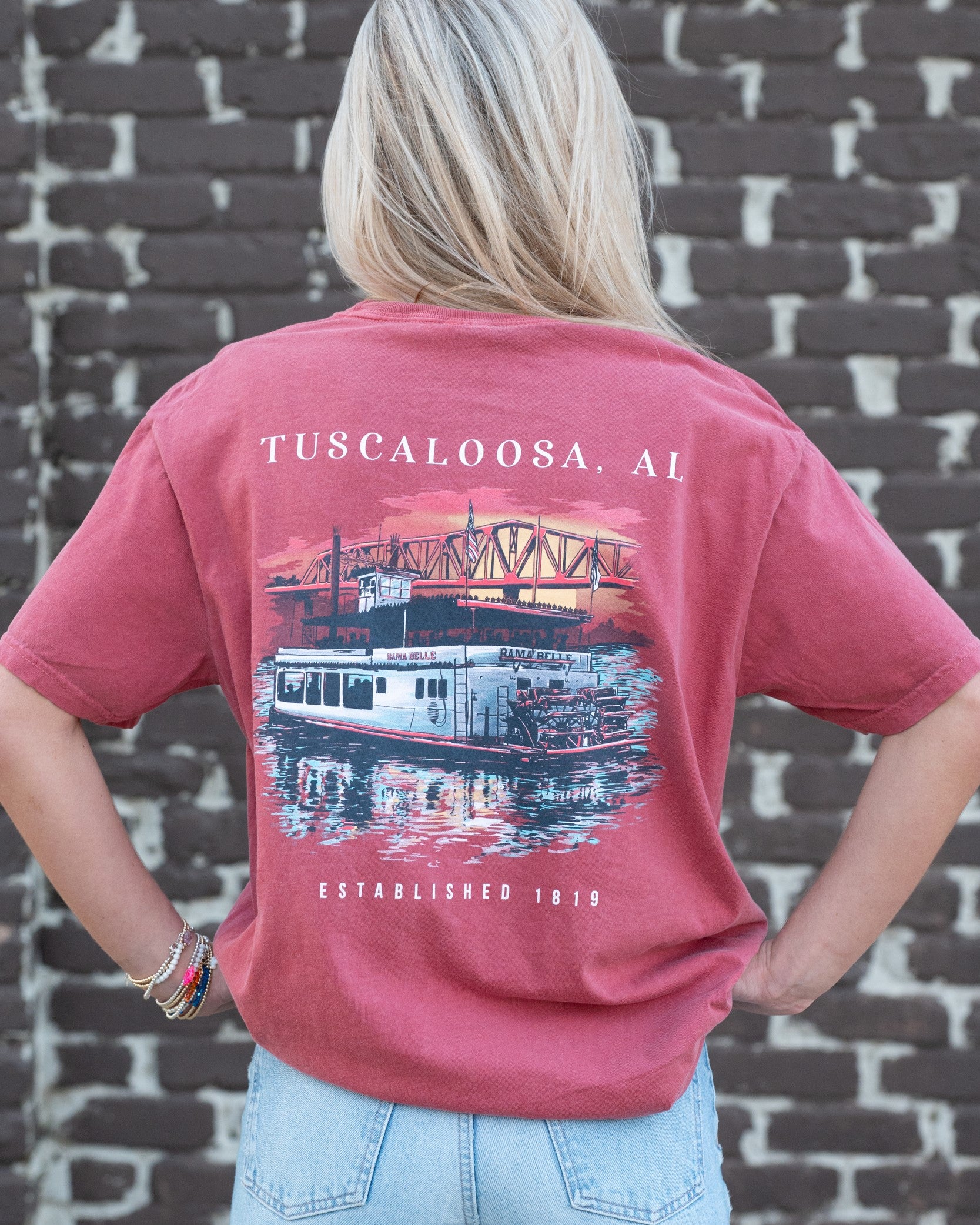 Tuscaloosa Red T-Shirt with White text "Tuscaloosa, AL" above  an illustration of a riverboat sailing underneath the Tuscaloosa Trestle as the sun sets