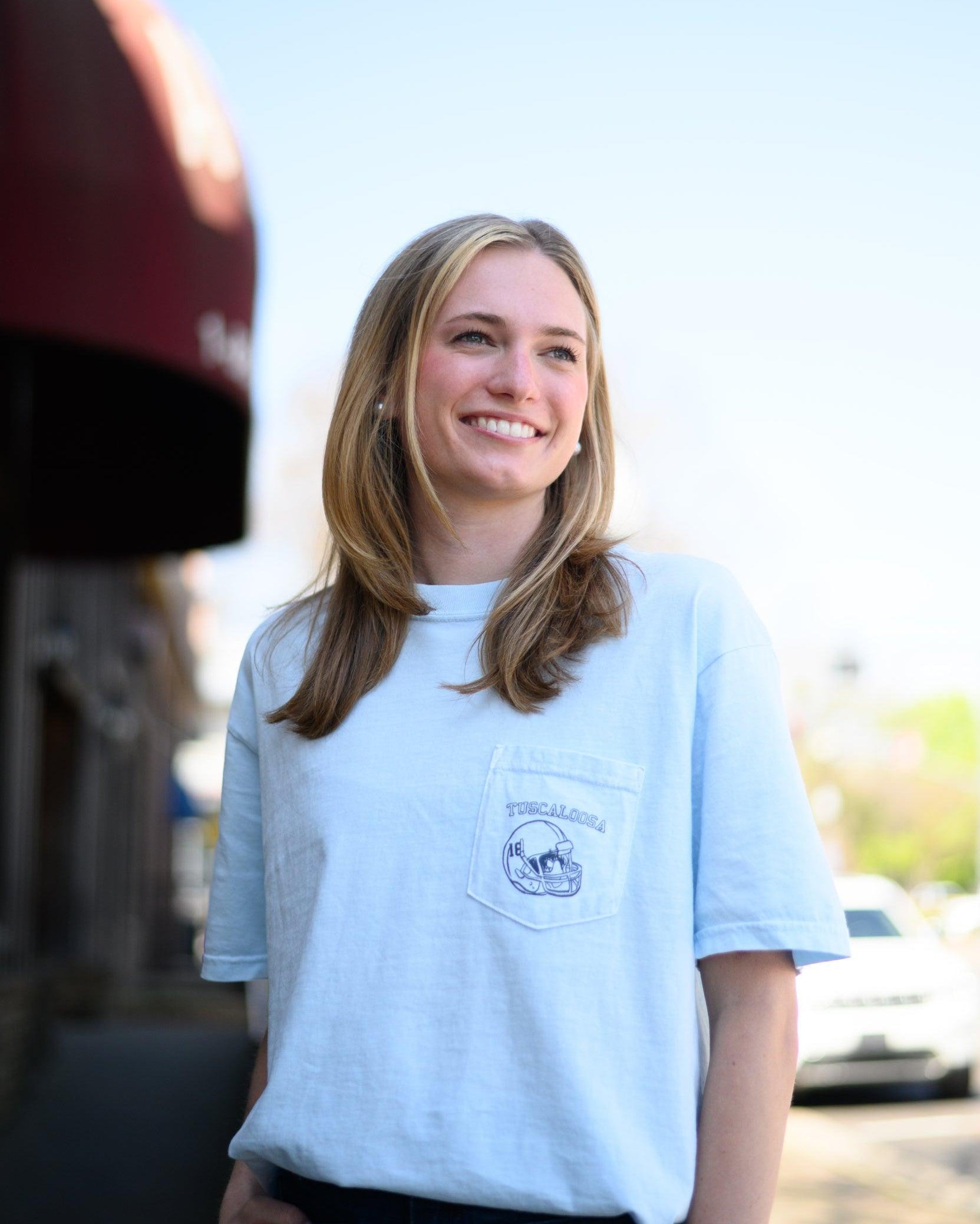 Local Merch Light Blue T-Shirt with a front pocket design featuring a football helmet and text “Tuscaloosa”