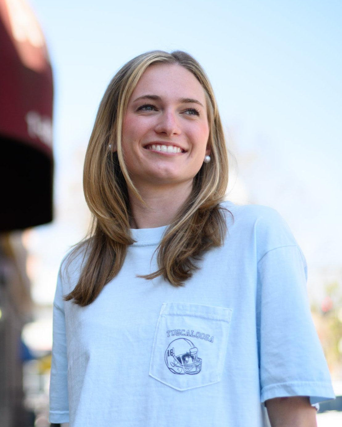 Local Merch Light Blue T-Shirt with a front pocket design featuring a football helmet and text “Tuscaloosa”