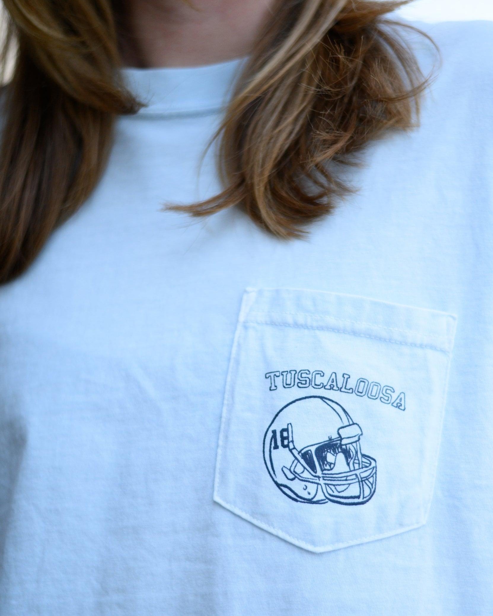 Local Merch Light Blue T-Shirt with a front pocket design featuring a football helmet and text “Tuscaloosa”