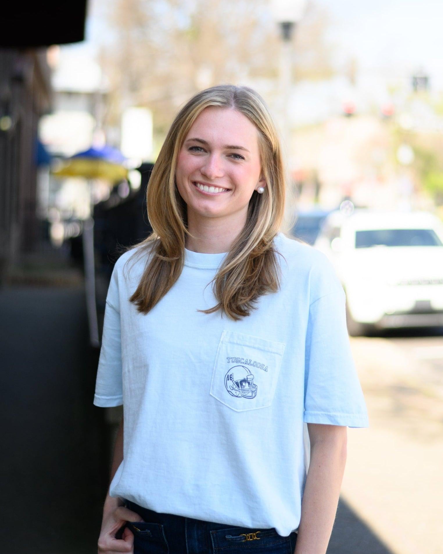 Local Merch Light Blue T-Shirt with a front pocket design featuring a football helmet and text “Tuscaloosa”