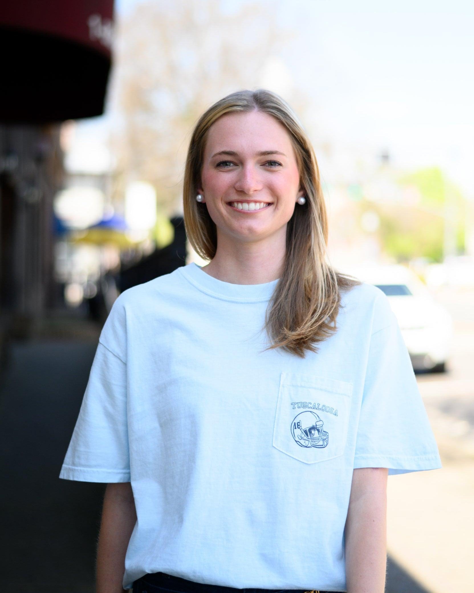 Local Merch Light Blue T-Shirt with a front pocket design featuring a football helmet and text “Tuscaloosa”
