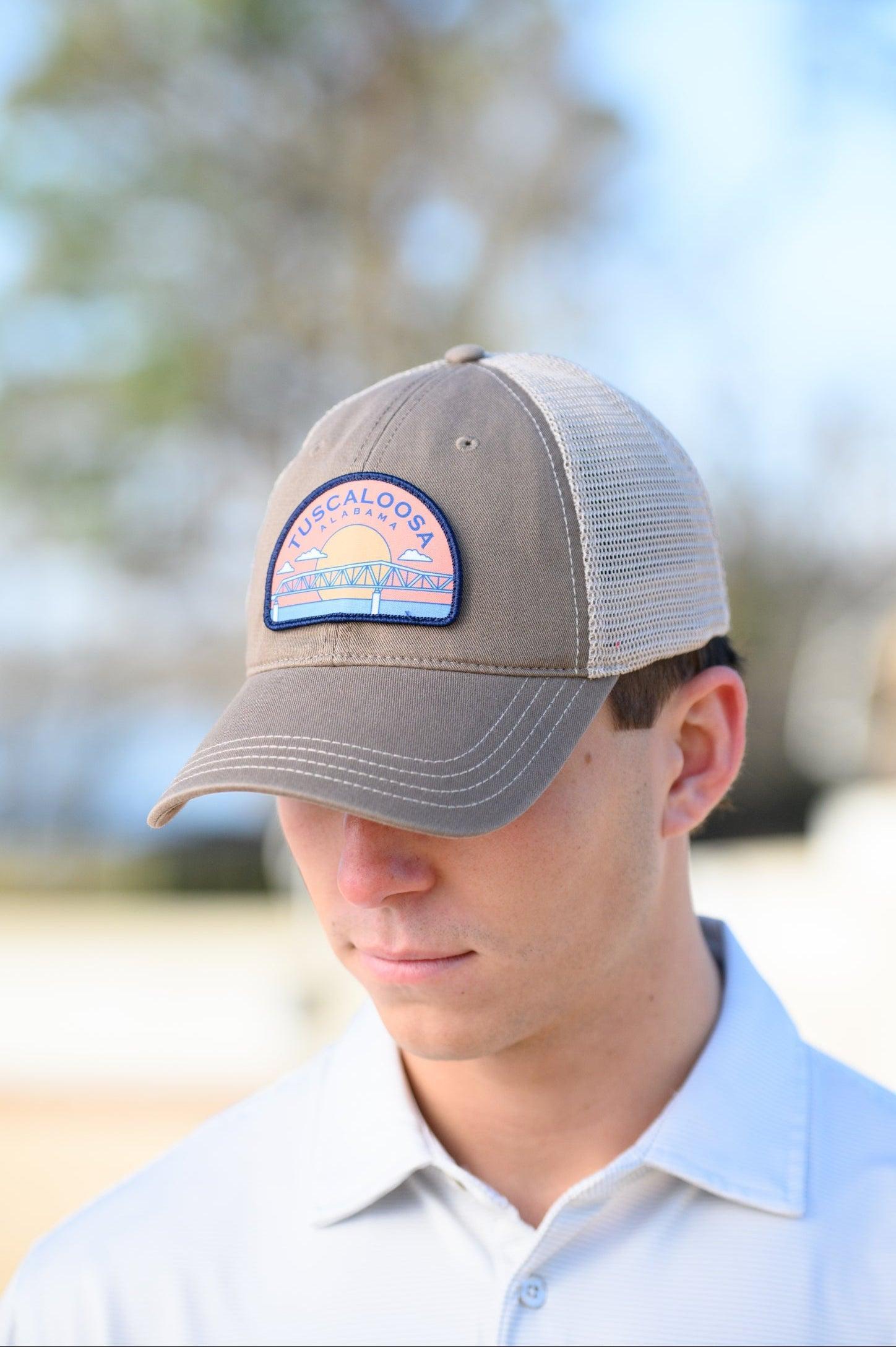 Tuscaloosa Beige Trucker Hat with a patch featuring Navy text "Tuscaloosa Alabama" a drawing of the sun setting on the iconic Tuscaloosa Trestle