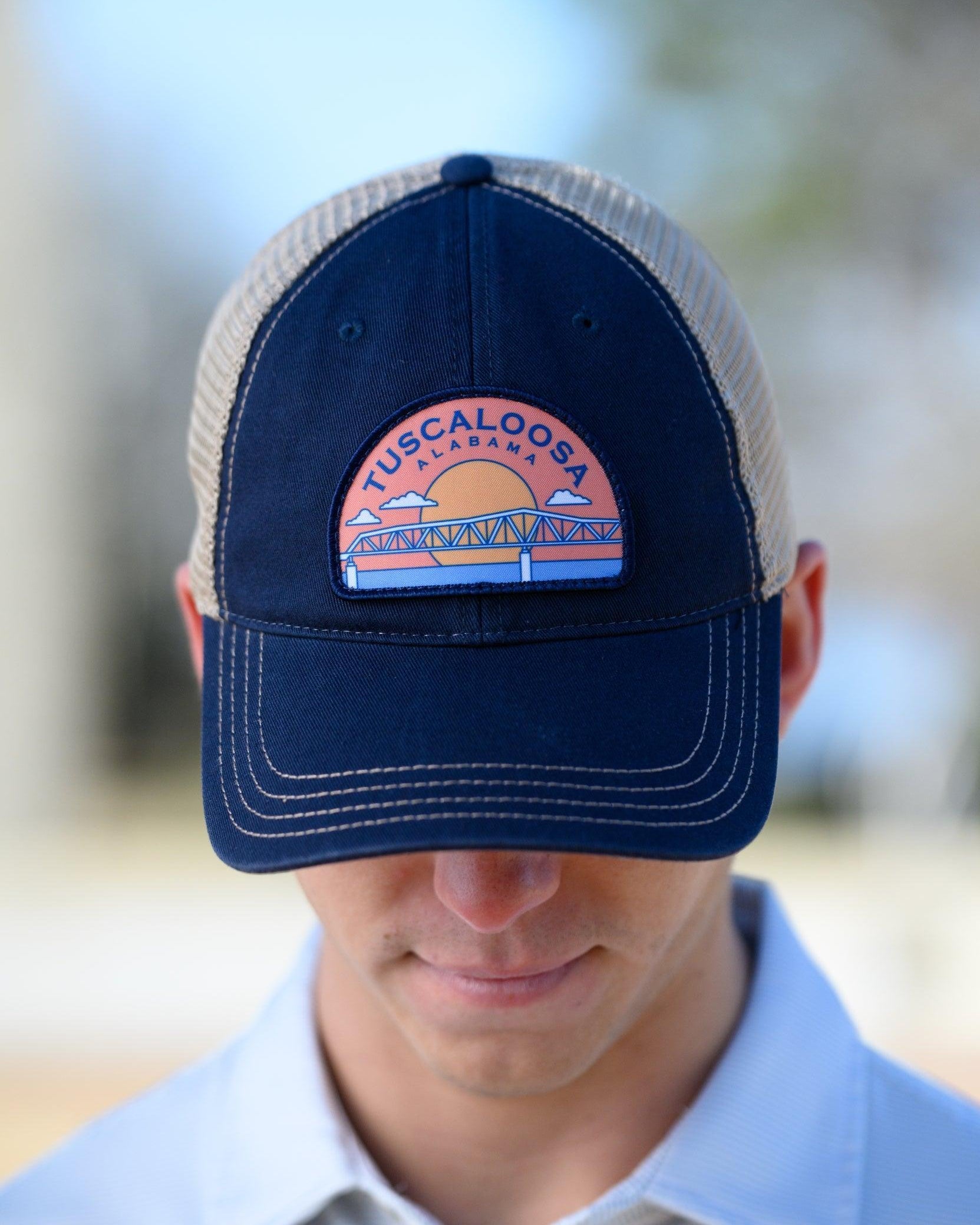 Tuscaloosa Navy and Beige Trucker Hat with a patch featuring Navy text "Tuscaloosa Alabama" a drawing of the sun setting on the iconic Tuscaloosa Railroad Tracks
