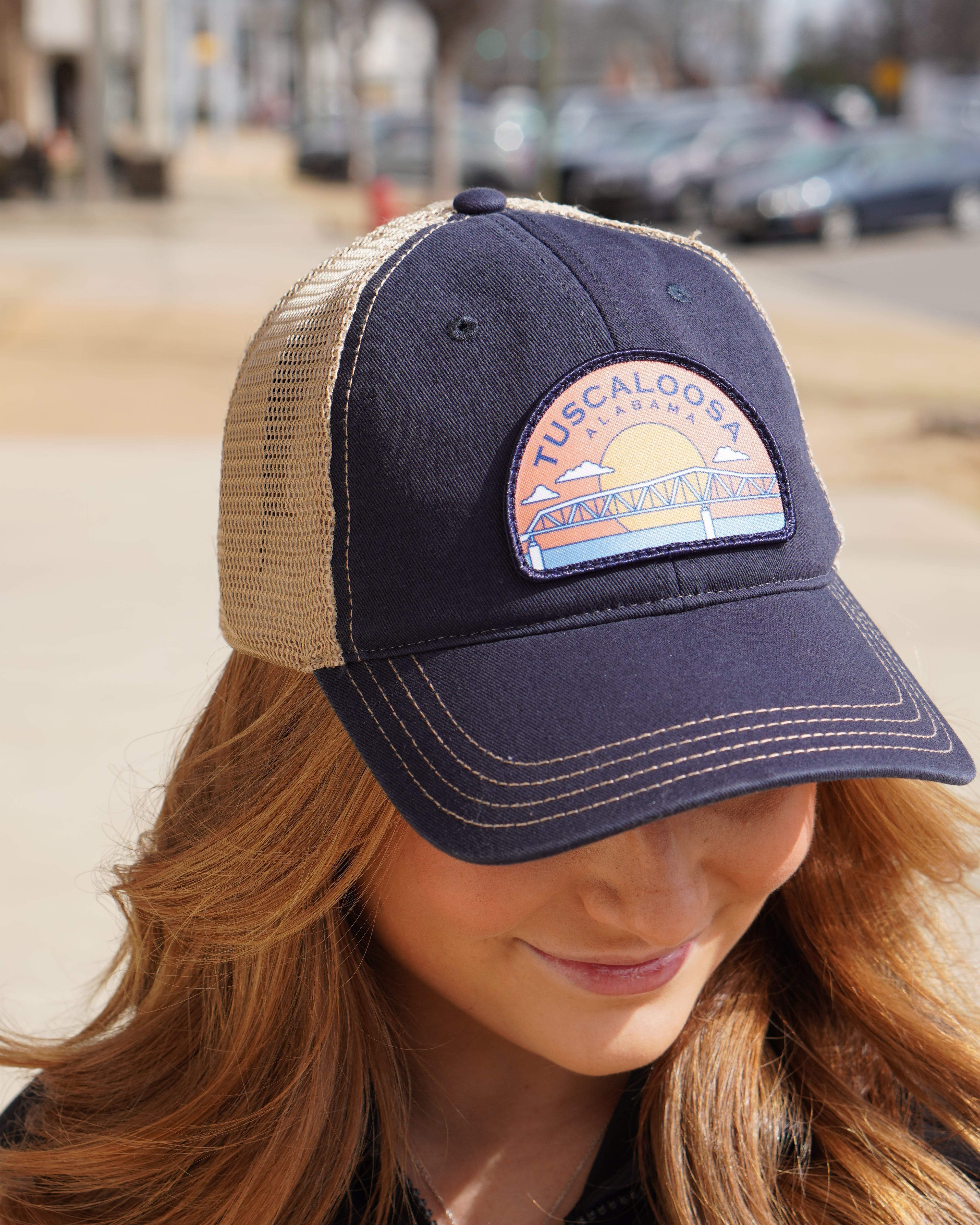 Tuscaloosa Navy and Beige Trucker Hat with a patch featuring Blue text "Tuscaloosa Alabama" a drawing of the sun setting on the iconic Tuscaloosa Railroad Tracks