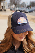 Tuscaloosa Navy and Beige Trucker Hat with a patch featuring Blue text "Tuscaloosa Alabama" a drawing of the sun setting on the iconic Tuscaloosa Railroad Tracks