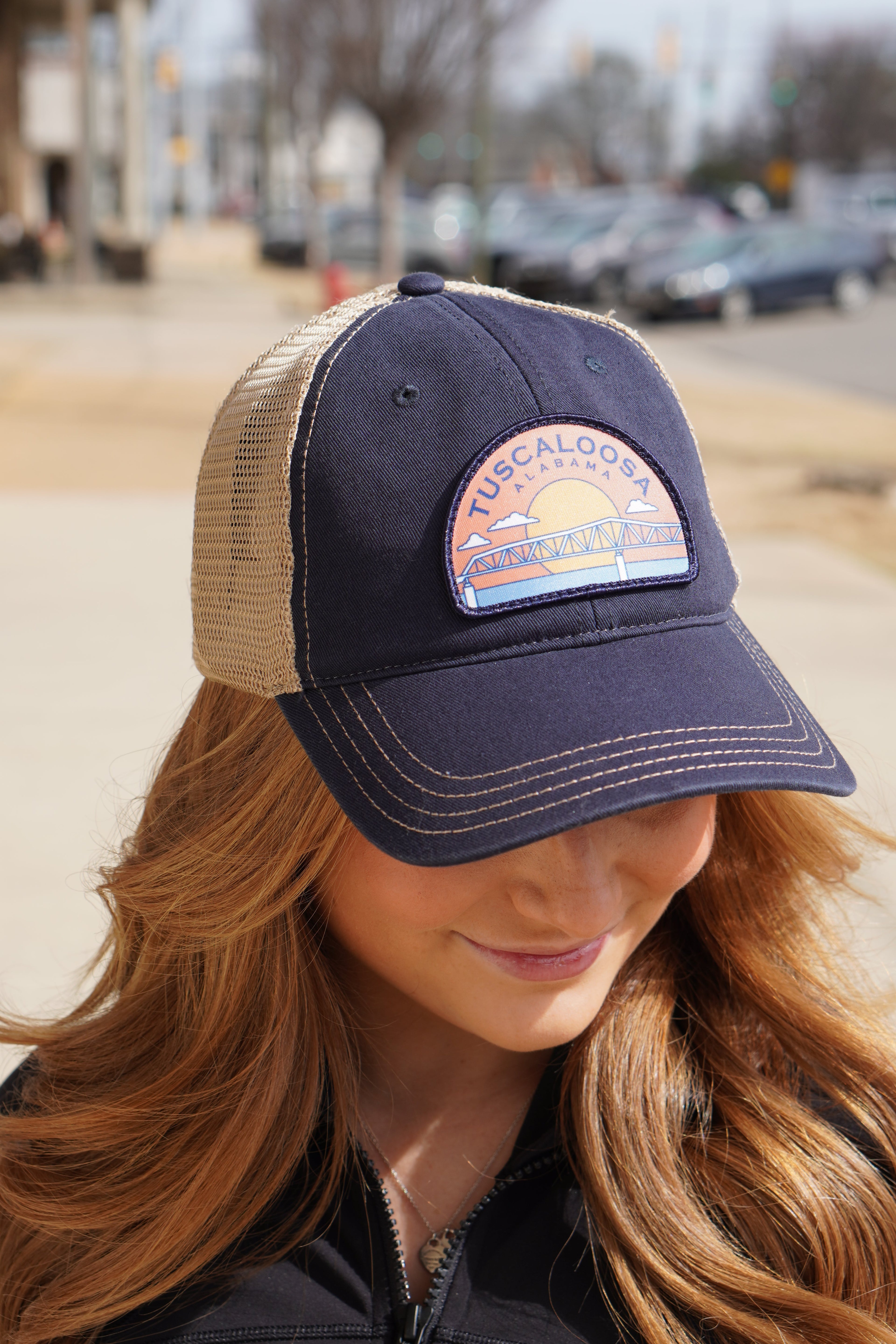 Tuscaloosa Navy and Beige Trucker Hat with a patch featuring Blue text "Tuscaloosa Alabama" a drawing of the sun setting on the iconic Tuscaloosa Railroad Tracks