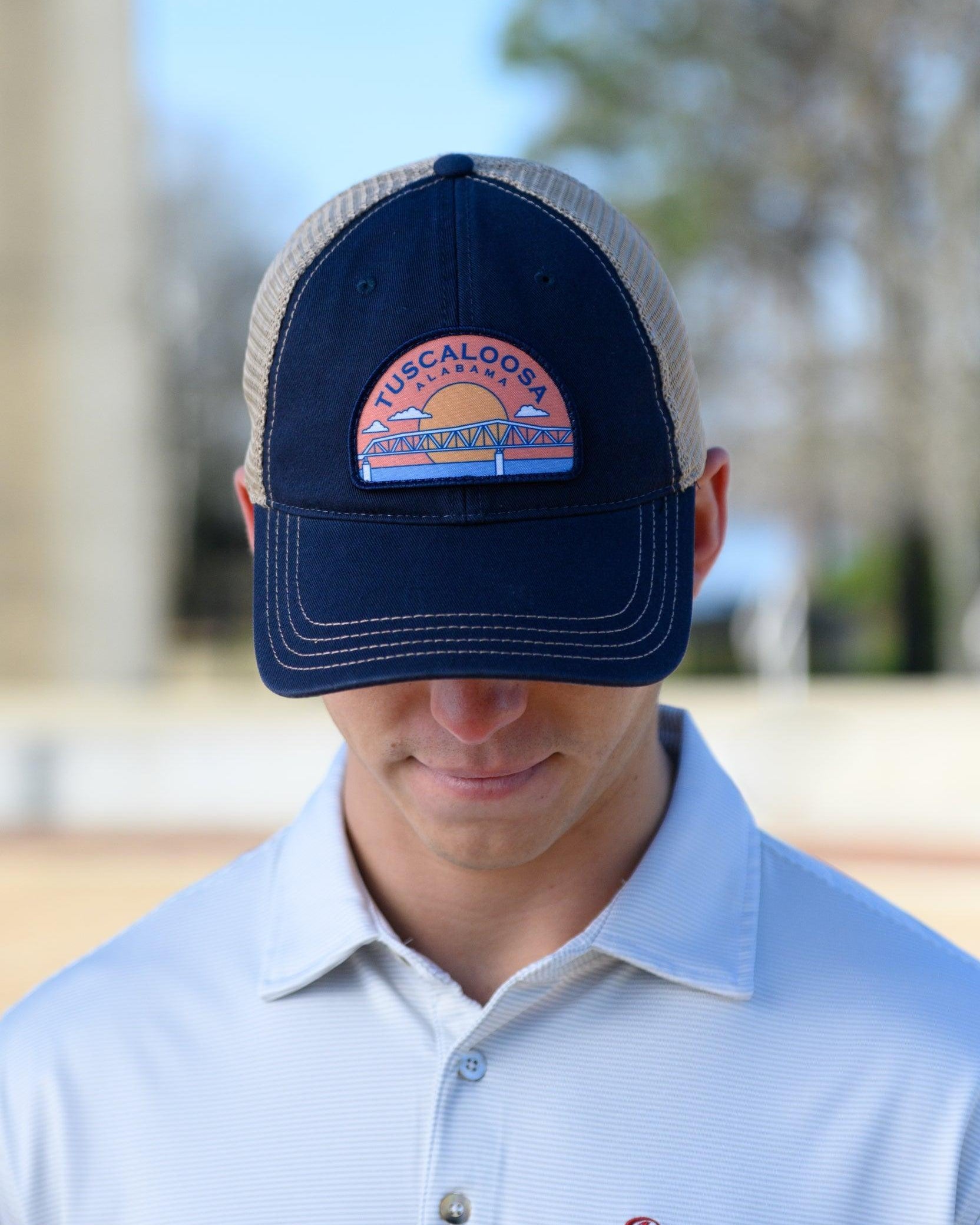 Tuscaloosa Navy and Beige Trucker Hat with a patch featuring Navy text "Tuscaloosa Alabama" a drawing of the sun setting on the iconic Tuscaloosa Railroad Tracks