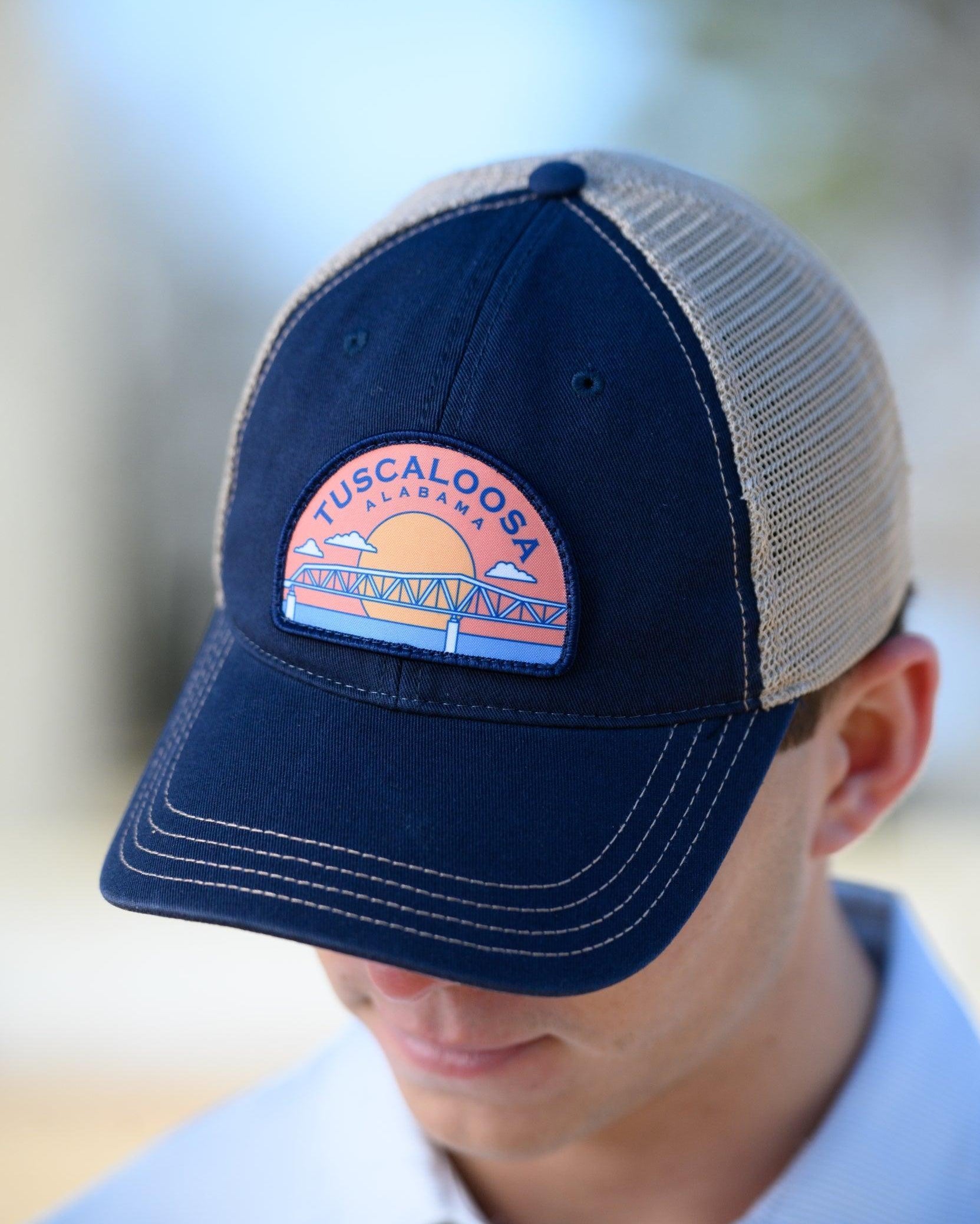 Tuscaloosa Navy and Beige Trucker Hat with a patch featuring Navy text "Tuscaloosa Alabama" a drawing of the sun setting on the iconic Tuscaloosa Railroad Tracks