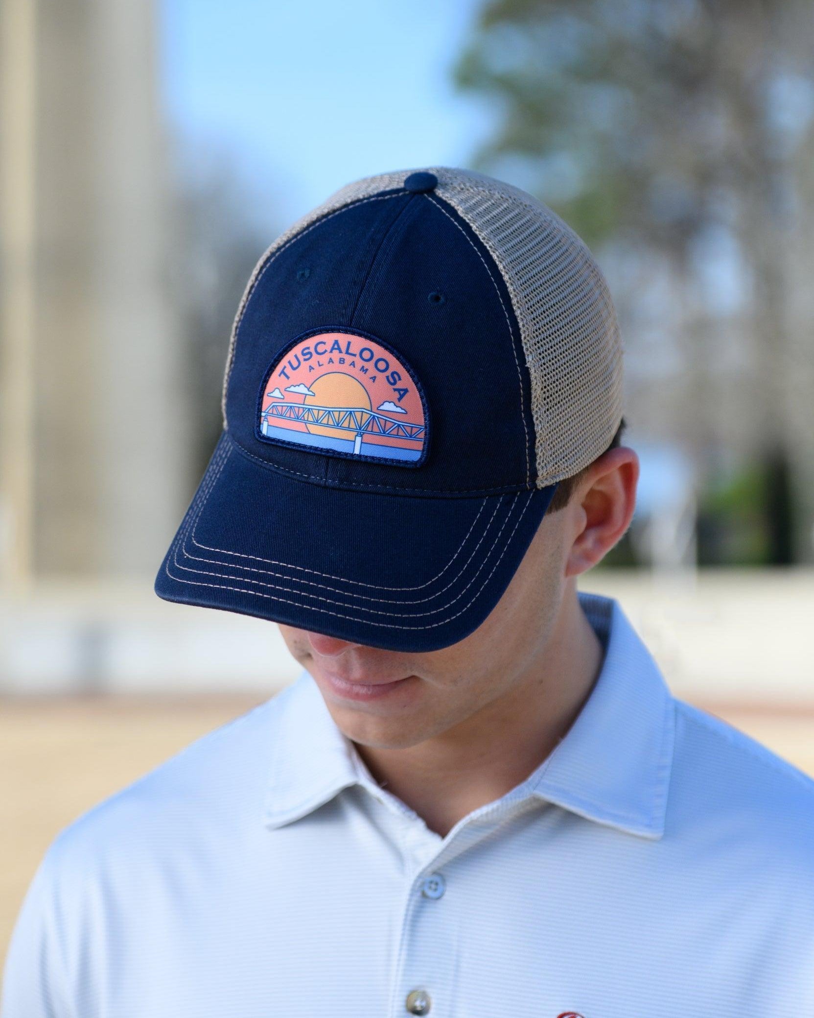 Tuscaloosa Navy and Beige Trucker Hat with a patch featuring Navy text "Tuscaloosa Alabama" a drawing of the sun setting on the iconic Tuscaloosa Railroad Tracks