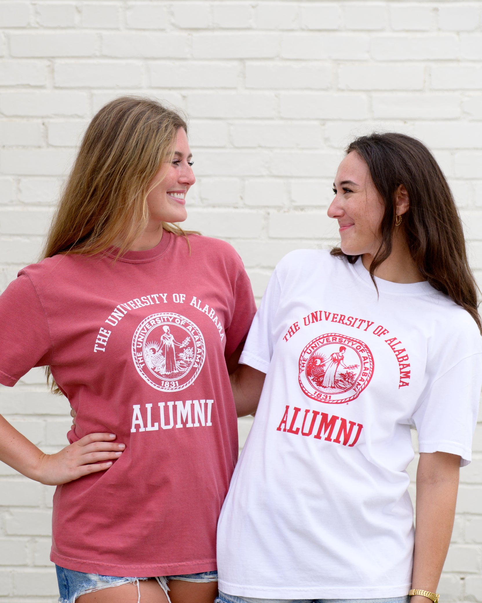 University of Alabama Red Alumni T-Shirt with White text "University of Alabama" above the White Alumni Seal and White text "Alumni" below and White Alumni T-Shirt with Red text "University of Alabama" above the Red Alumni Seal and Red text "Alumni"