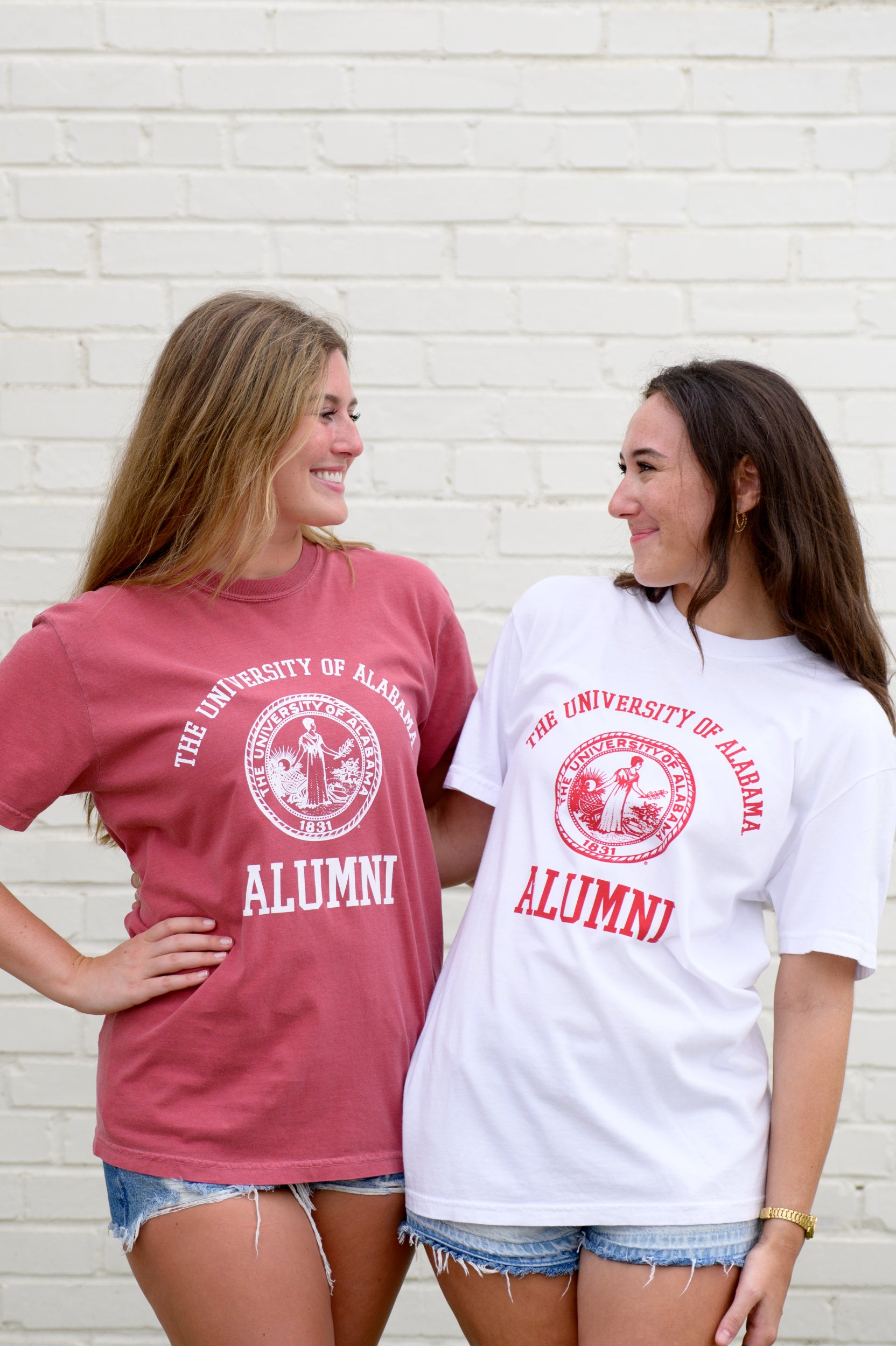 University of Alabama Red Alumni T-Shirt with White text "University of Alabama" above the White Alumni Seal and White text "Alumni" below and White Alumni T-Shirt with Red text "University of Alabama" above the Red Alumni Seal and Red text "Alumni"