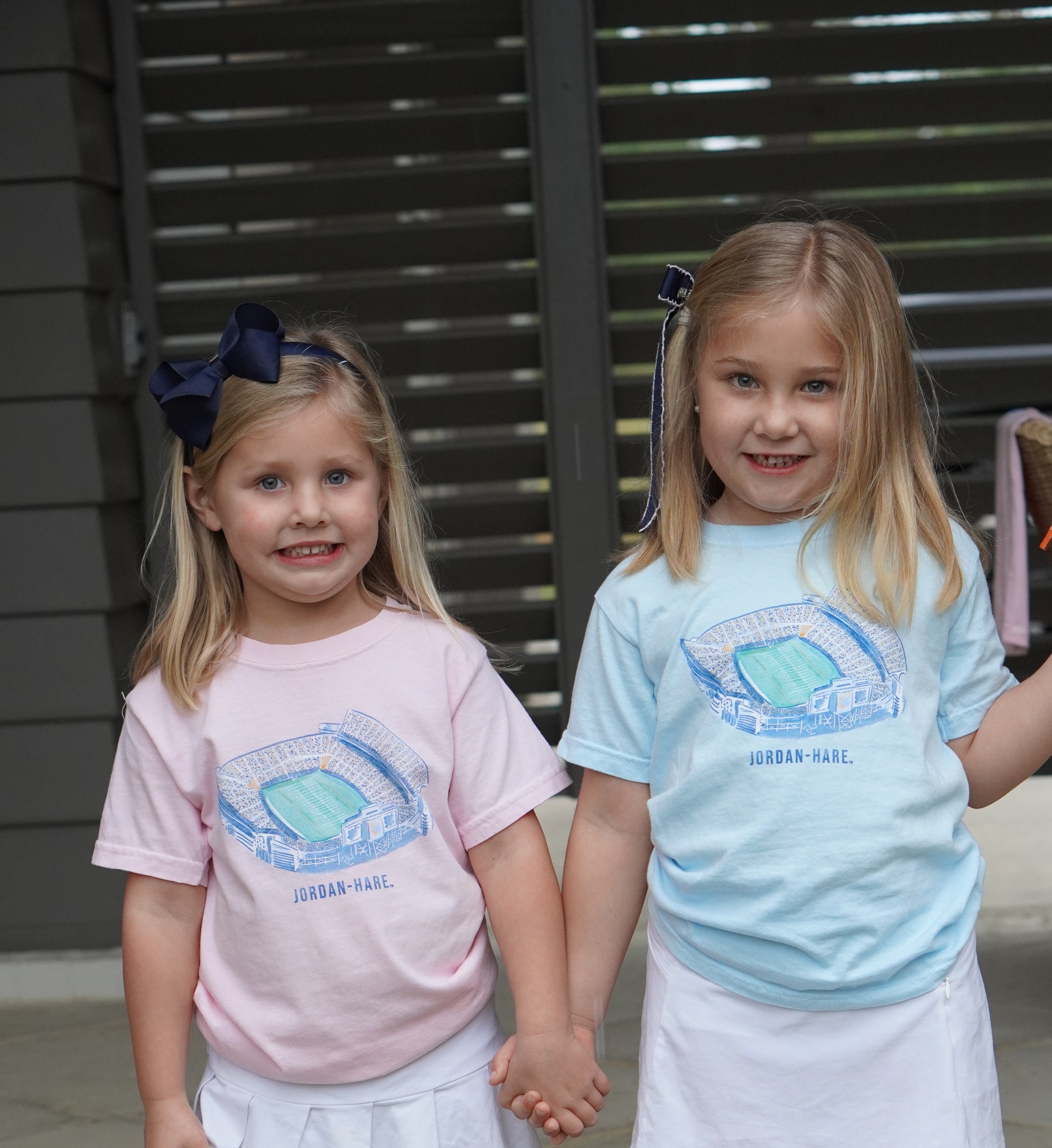 Auburn University Light Pink and Light Blue Youth T-Shirts with a watercolor illustration of Jordan-Hare Stadium