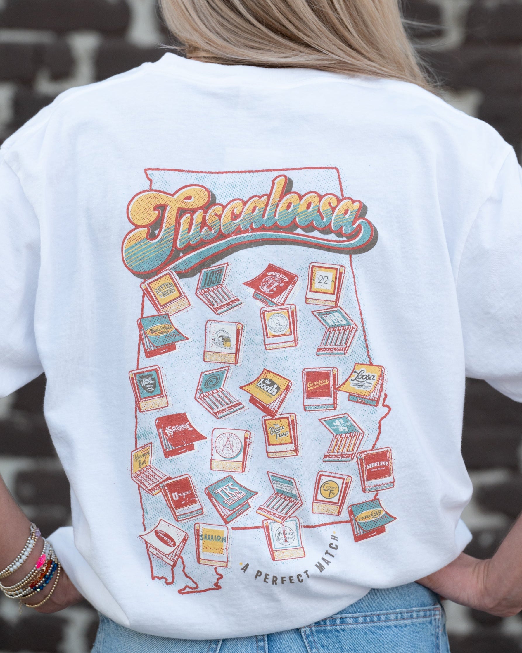 A Perfect Match White  Comfort Colors T-Shirt  with the text "Tuscaloosa" and images of matchbooks inside of an outline of the state of Alabama and smaller text reading "A PERFECT MATCH" outside the outline (Back)