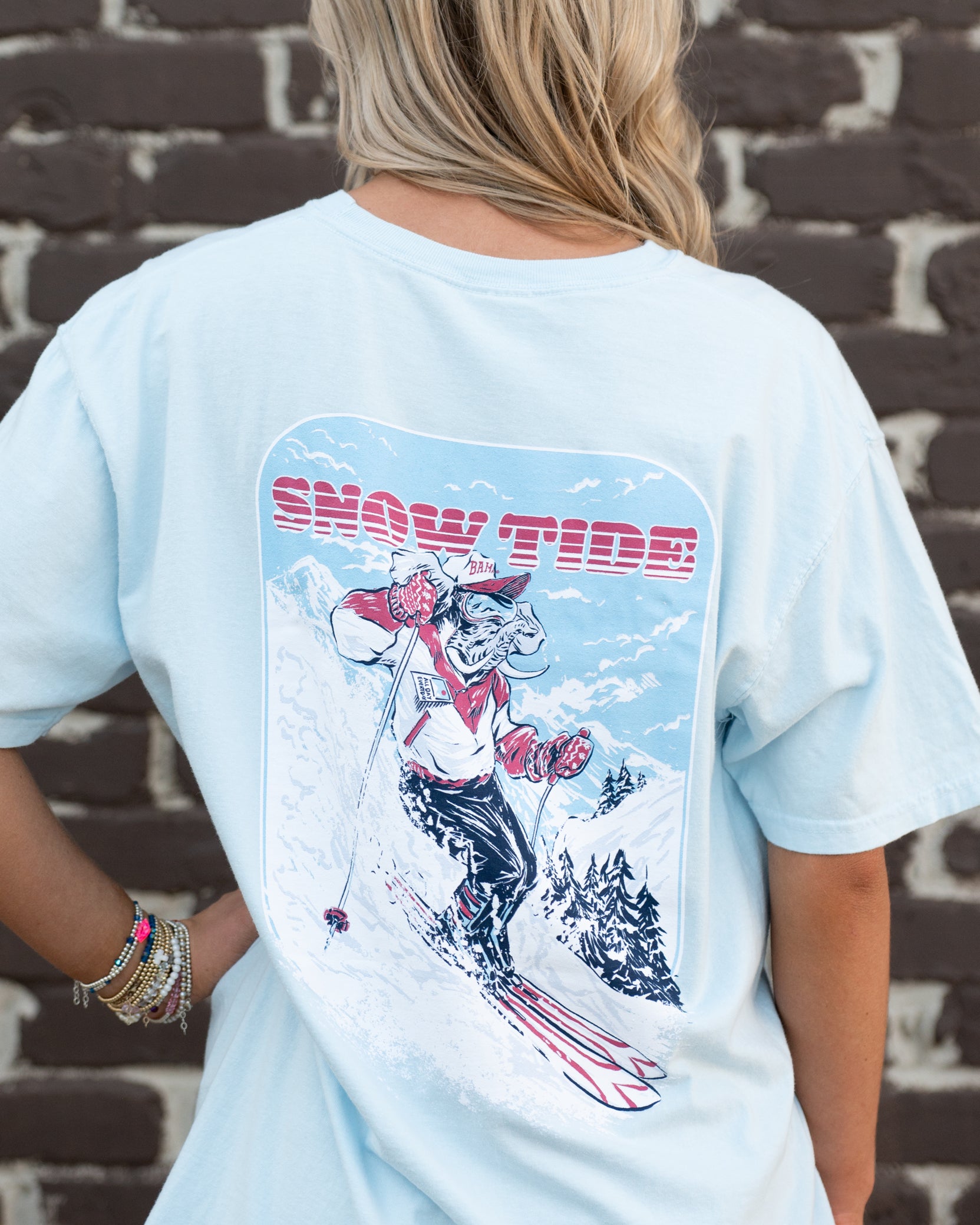 University of Alabama Big Al Snow Skiing Chambray Comfort Colors T-Shirt with text "Snow Tide" above an image of Big Al in a ski outfit skiing down a snow-covered mountain