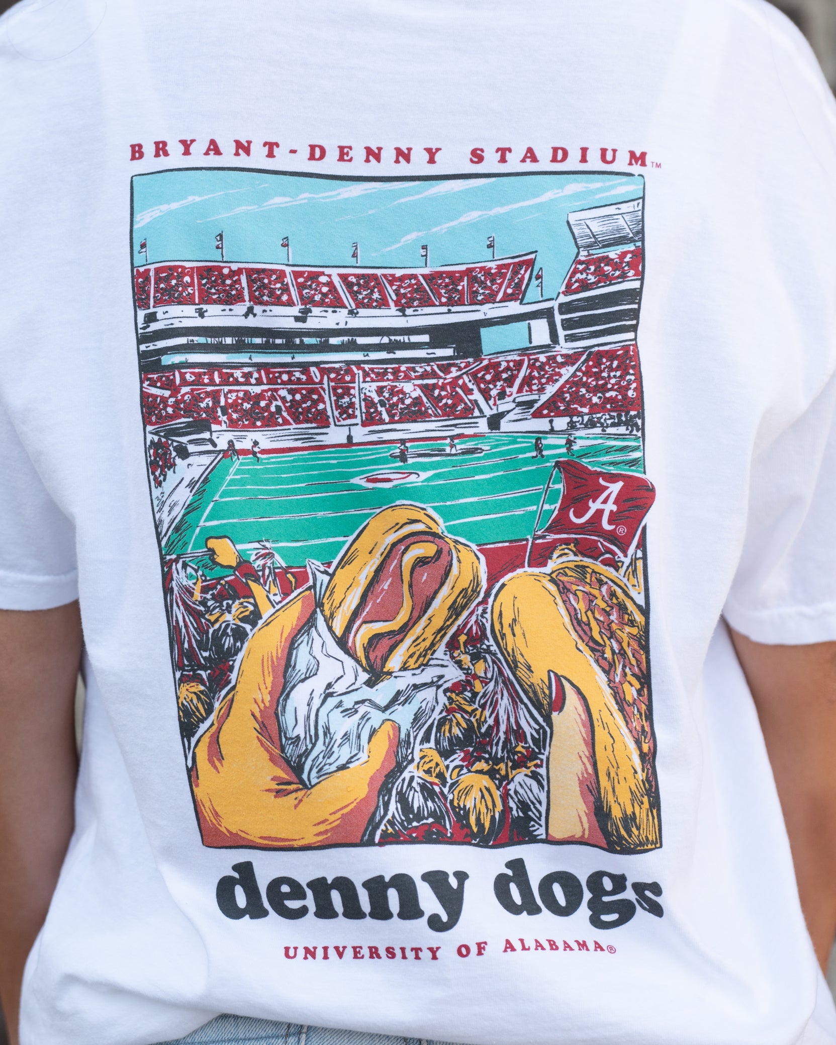 University of Alabama White Denny Dogs Comfort Colors T-Shirt with an image of two hands holding hot dogs at Bryant- Denny Stadium above the Black text "denny dogs"