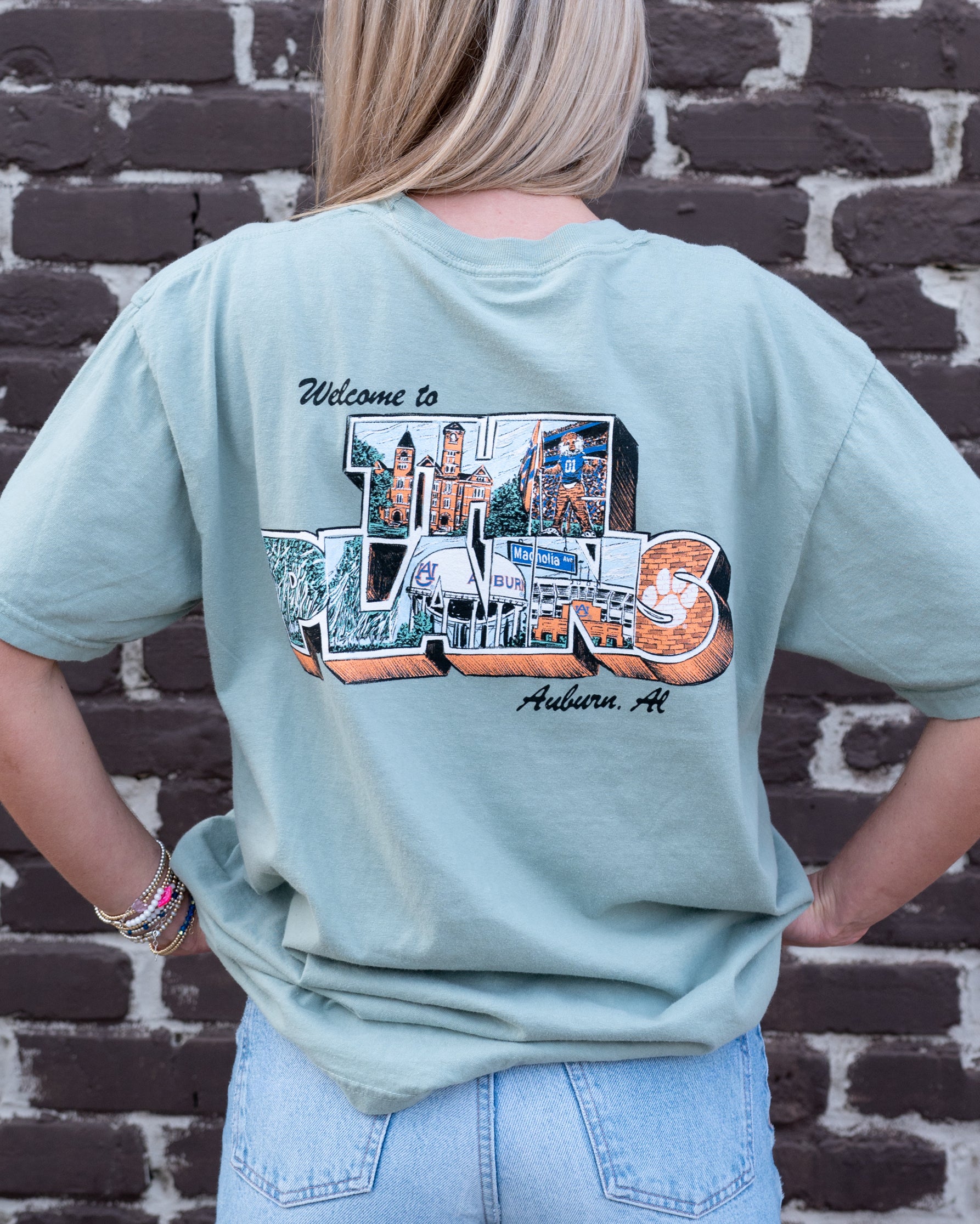 Auburn University Green The Plains T-Shirt with postcard style text "Welcome to THE PLAINS" with "The Plains" filled with images of iconic buildings in that location