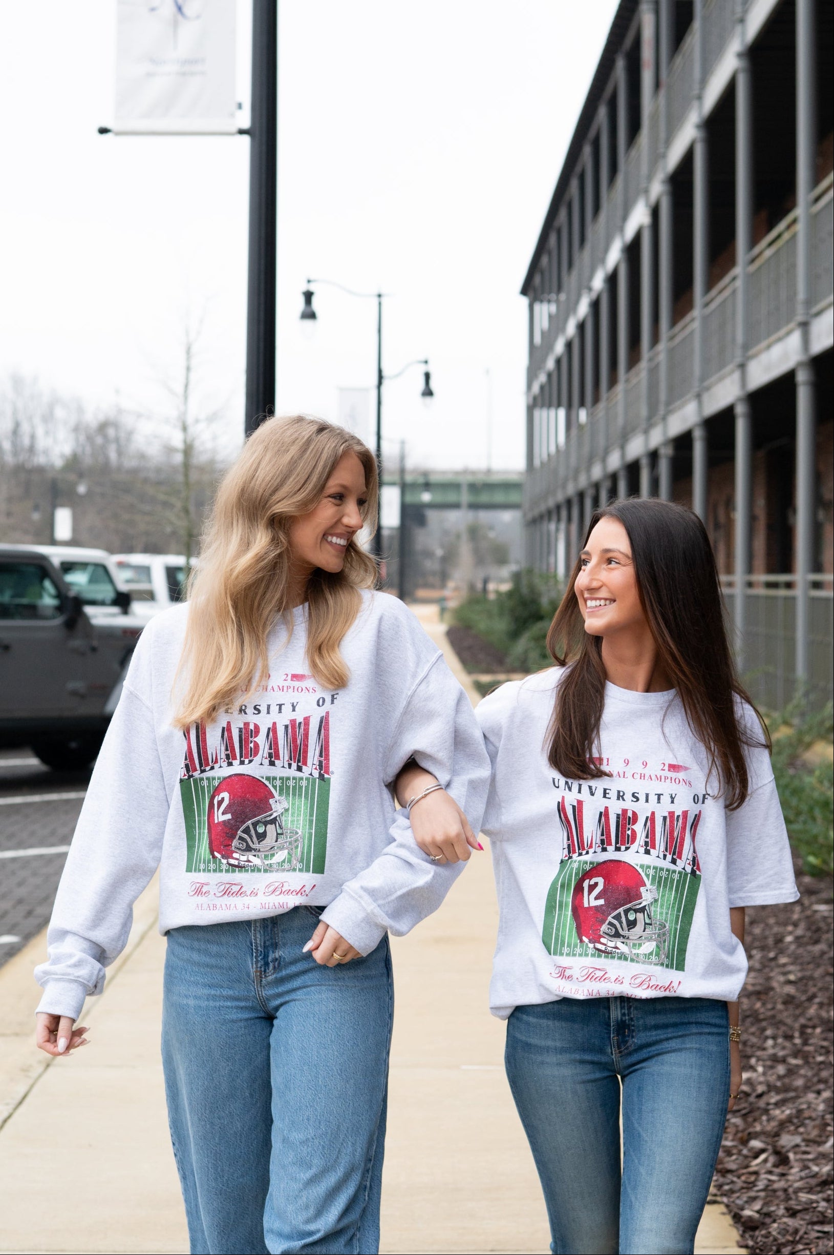 Two women wearing matching University of Alabama sweatshirts walking outdoors.