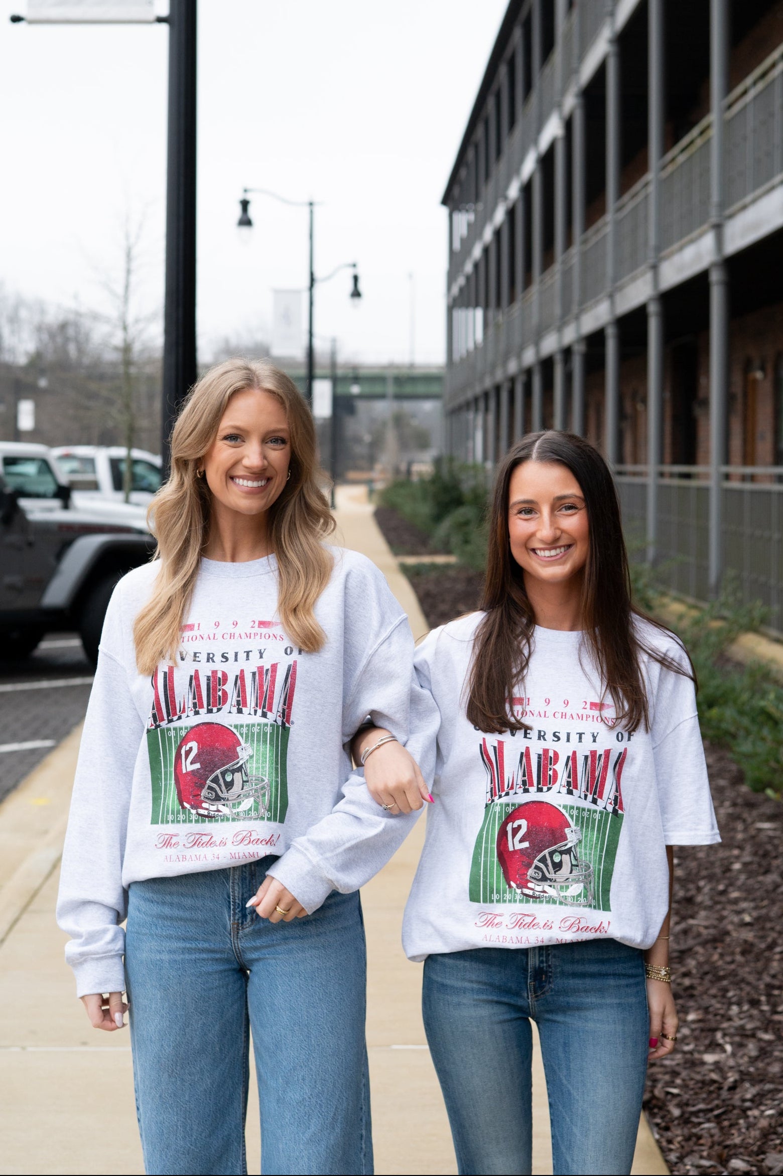 Two women wearing matching sweatshirts with a graphic design on a street.