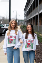 Two women wearing matching sweatshirts with a graphic design on a street.