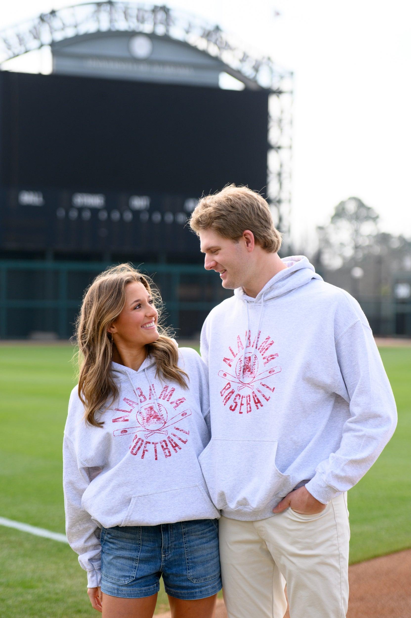 Two people wearing white hoodies with red text on a baseball field.