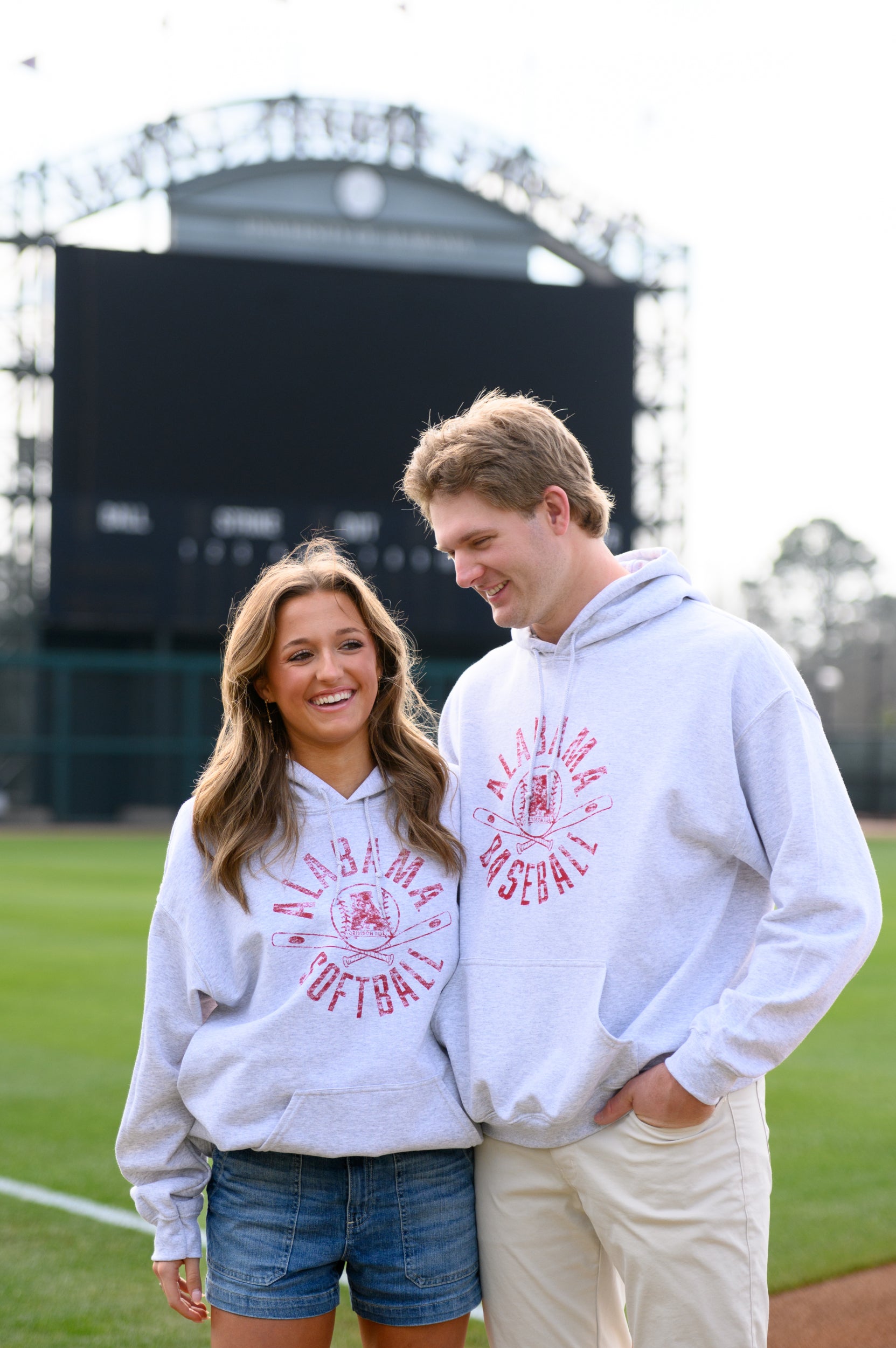 Two people wearing matching white hoodies with red text on a sports field.