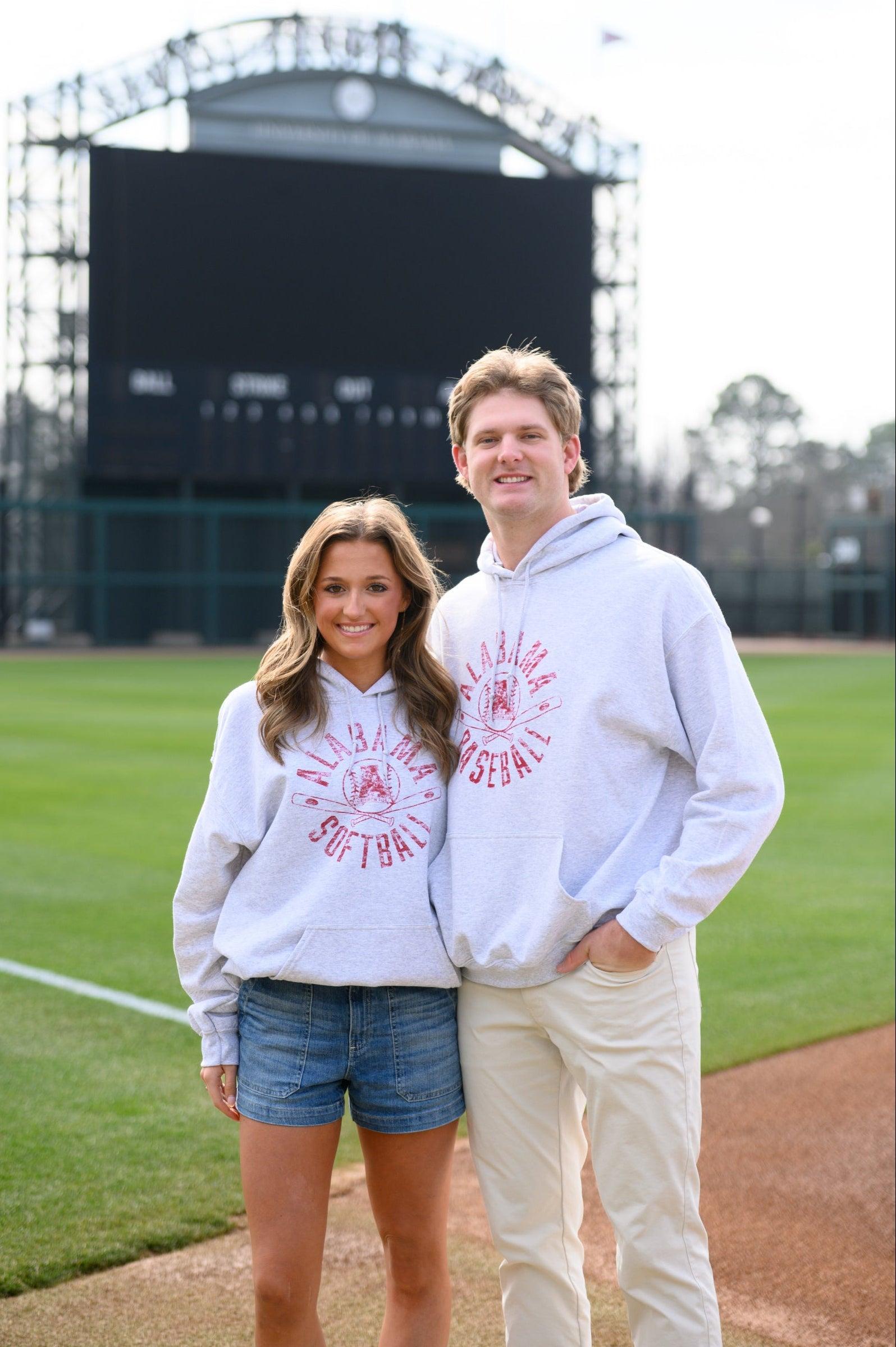 Two people wearing matching sweatshirts on a baseball field