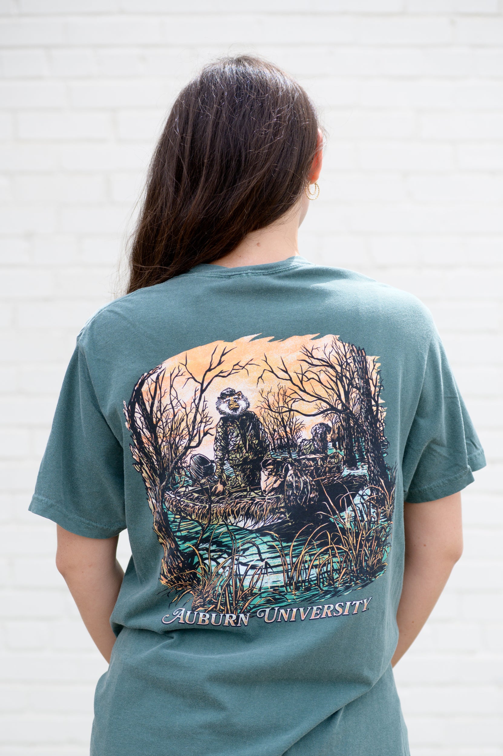 Auburn University Aubie Duck Hunt Blue Spruce Comfort Colors T-Shirt with an image of Aubie the Tiger wearing hunting gear with a dog in a boat in the swamp 