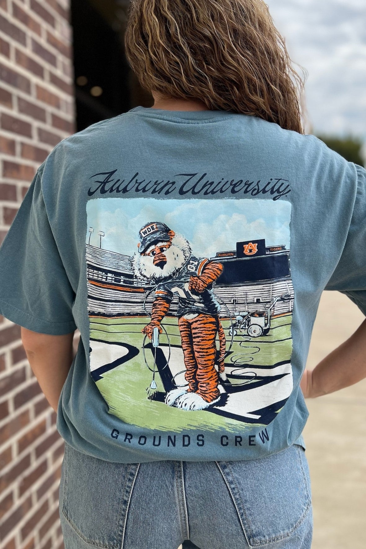 Auburn University Aubie Grounds Crew Ice Blue Comfort Colors T-Shirt with an image of Aubie the Tiger wearing a hat and painting the turf on the football field