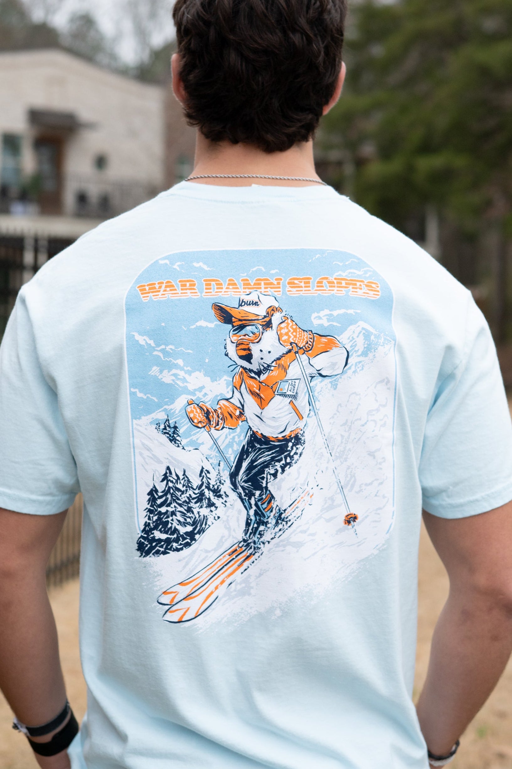 Auburn University Aubie Snow Skiing Chambray Comfort Colors T-Shirt with text "War Damn Slopes" above an image of Aubie in a ski outfit skiing down a snow-covered mountain