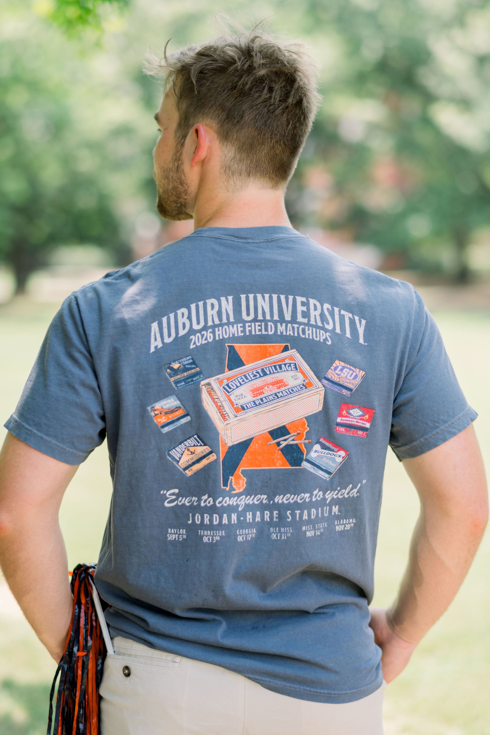 Auburn University Dusty Navy T-Shirt with White Text “2026 Home Field Matchups,” and illustrations of matchbooks. One large “The Plains” matchbook is surrounded by matchbooks from (listed left to right): Southern Miss, Florida Gators, Vanderbilt, Samford, Razorback, and LSU