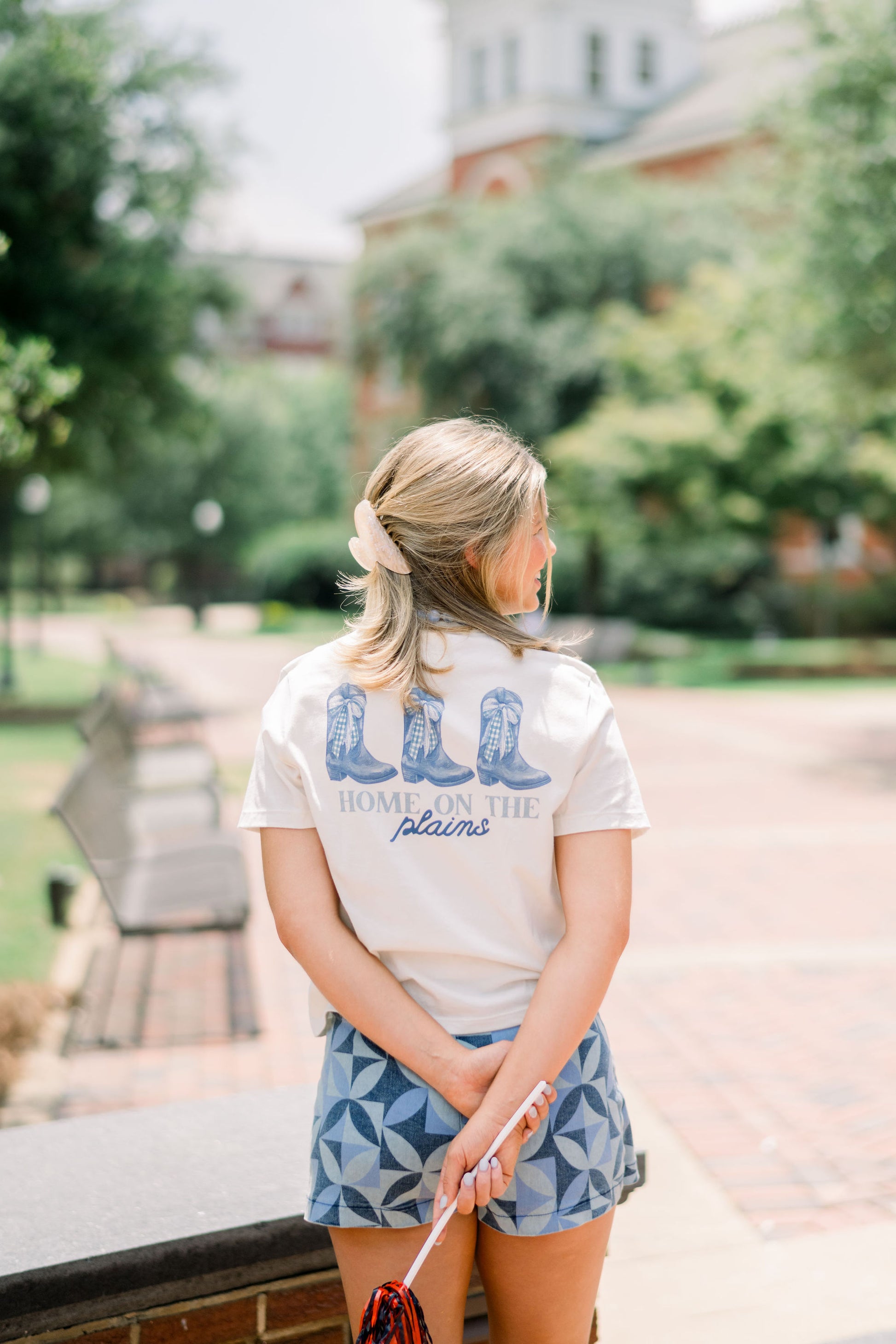 Auburn University White Ladies Tee with a vintage Blue illustration of cowgirl boots with bows tied on them above Blue text “Home On The Plains”