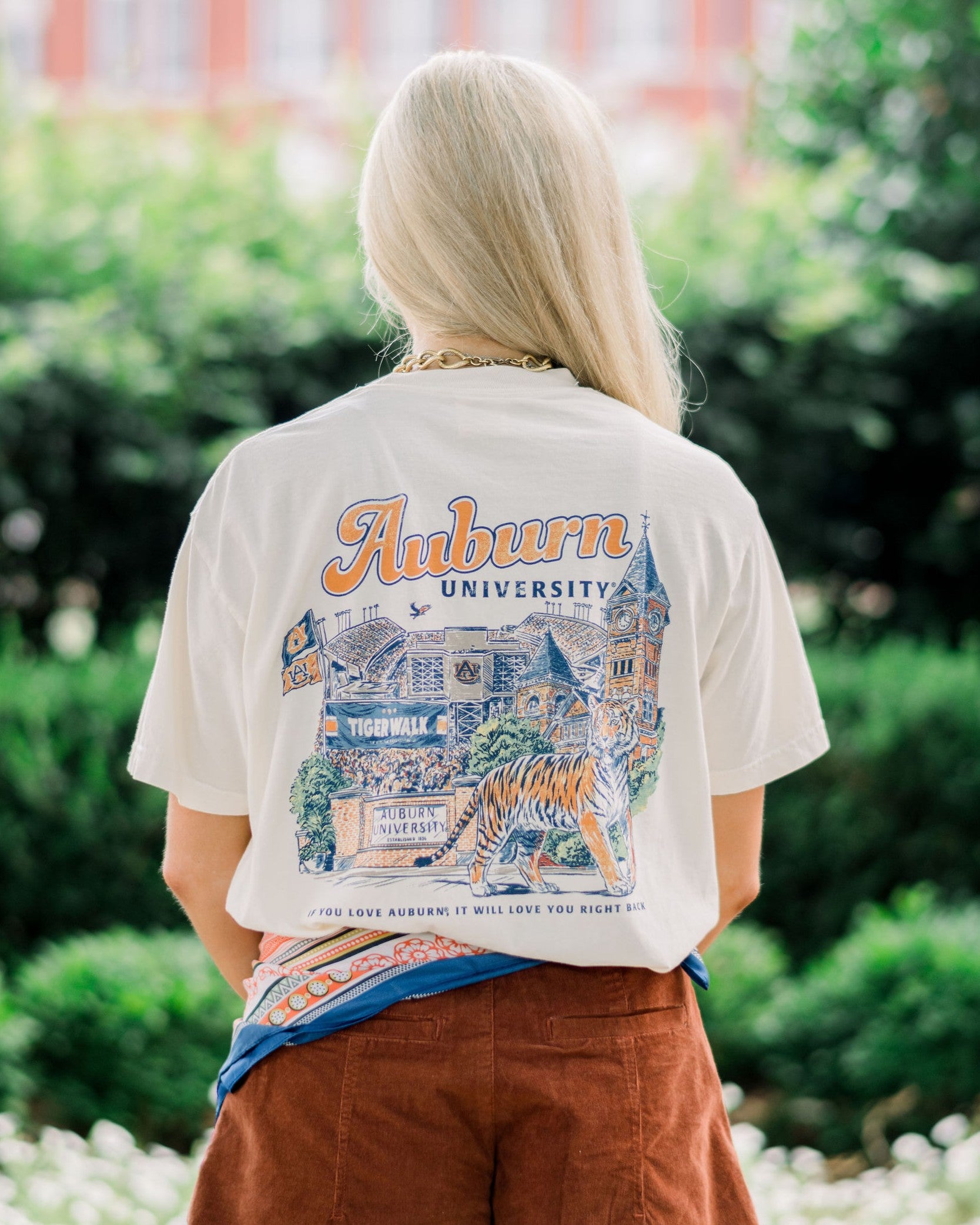 Auburn University Ivory T-Shirt with text “Auburn University” above an illustration of a tiger prowling in front of a collage of auburn icons such as Sanford Hall, Jordan Hare Stadium, and Tiger Walk
