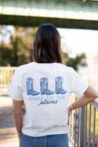 Auburn University White Ladies Tee with a vintage Blue illustration of cowgirl boots with bows tied on them above Blue text “Home On The Plains”